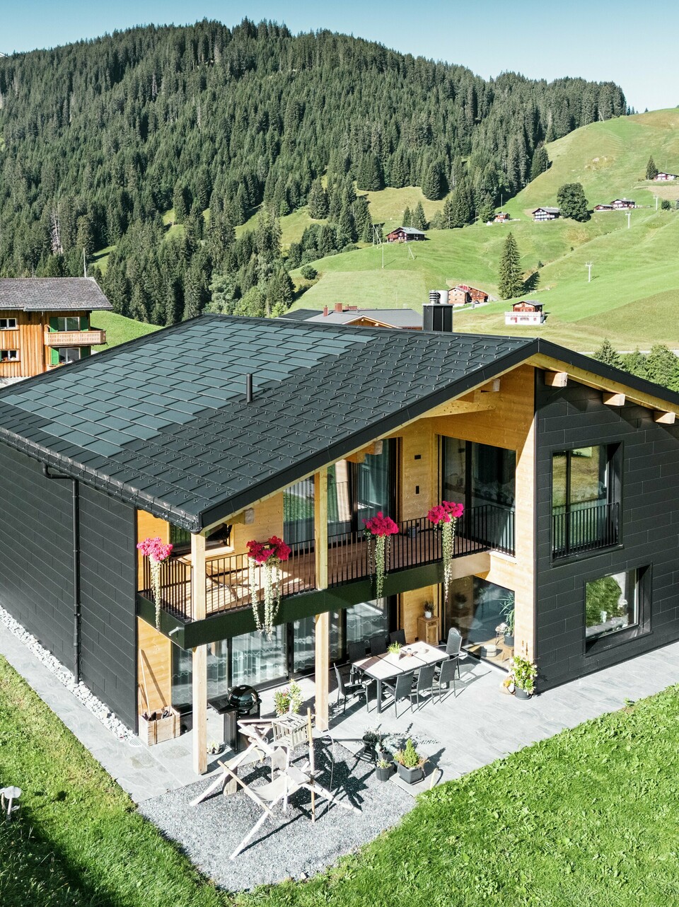 Elegantna enodružinska hiša v hribovitem okolju Ascharina (Švica) kaže, kako se lahko aluminij in les odlično združita. Robustni fasadni paneli PREFA Siding.X v črni barvi P.10 so usklajeni s streho iz solarnih strešnih plošč PREFA in strešnih plošč R.16 v enakem barvnem premazu. Trpežna aluminijasta obloga zanesljivo ščiti stavbo pred izzivi alpskega podnebja.