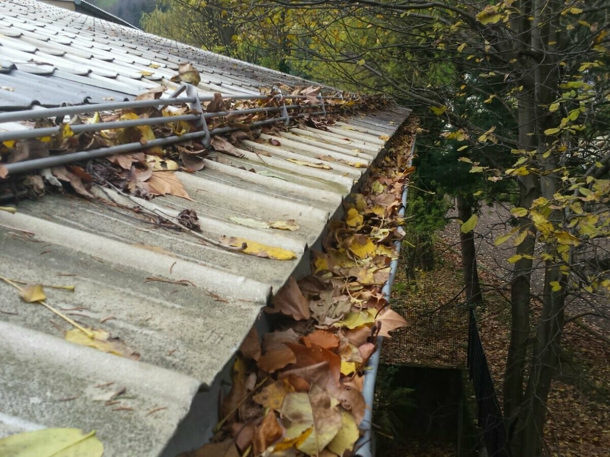 Strešni žleb z veliko jesenskega listja, čiščenje zamašenih žlebov