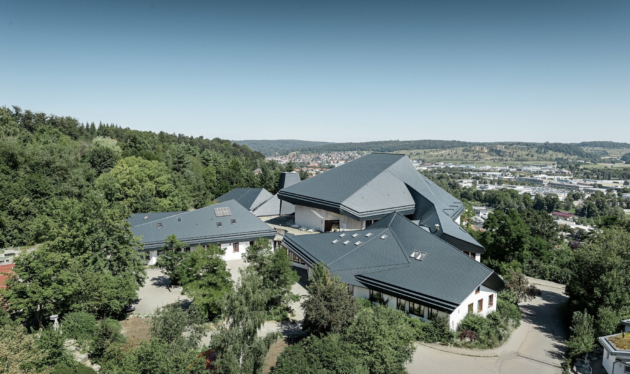 Valdorfska šola v Heidenheimu z novo sanirano streho; velika strešna površina z veliko koti in nakloni je pokrita s strešnimi skodlami PREFA v antracitni barvi