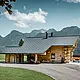Brunarica v Gosau-u v Avstriji s strešnim sistemom PREFA v antracitni barvi. Preizkušene strešne plošče R.16 ustvarjajo privlačen kontrast naravnemu lesu brunarice. V ozadju je veličastna gorska panorama, ki poudarja mirno in slikovito lokacijo hiše. Podrobna fotografija prikazuje simbiozo tradicionalne avstrijske arhitekture in sodobne strešne tehnologije ter prikazuje robustno in estetsko kakovost aluminijastih izdelkov PREFA.