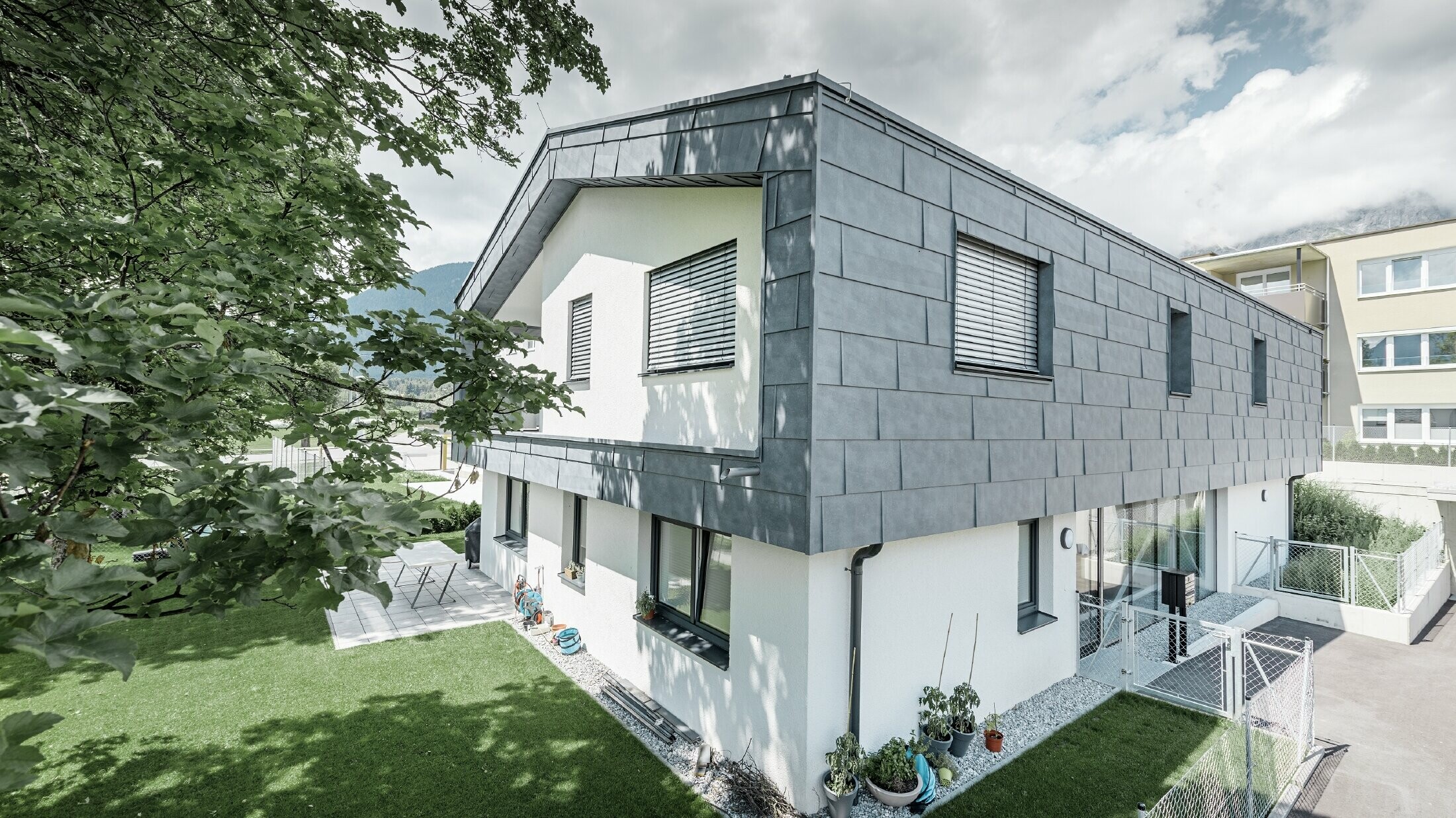 Sodobna nadgradnja stanovanjske hiše s ploščatim dvokapnim strešnim nadstreškom brez strešnega previsa; fasadna obloga je bila izvedena s PREFA fasadnim panelom FX.12 v kamnito sivi barvi.