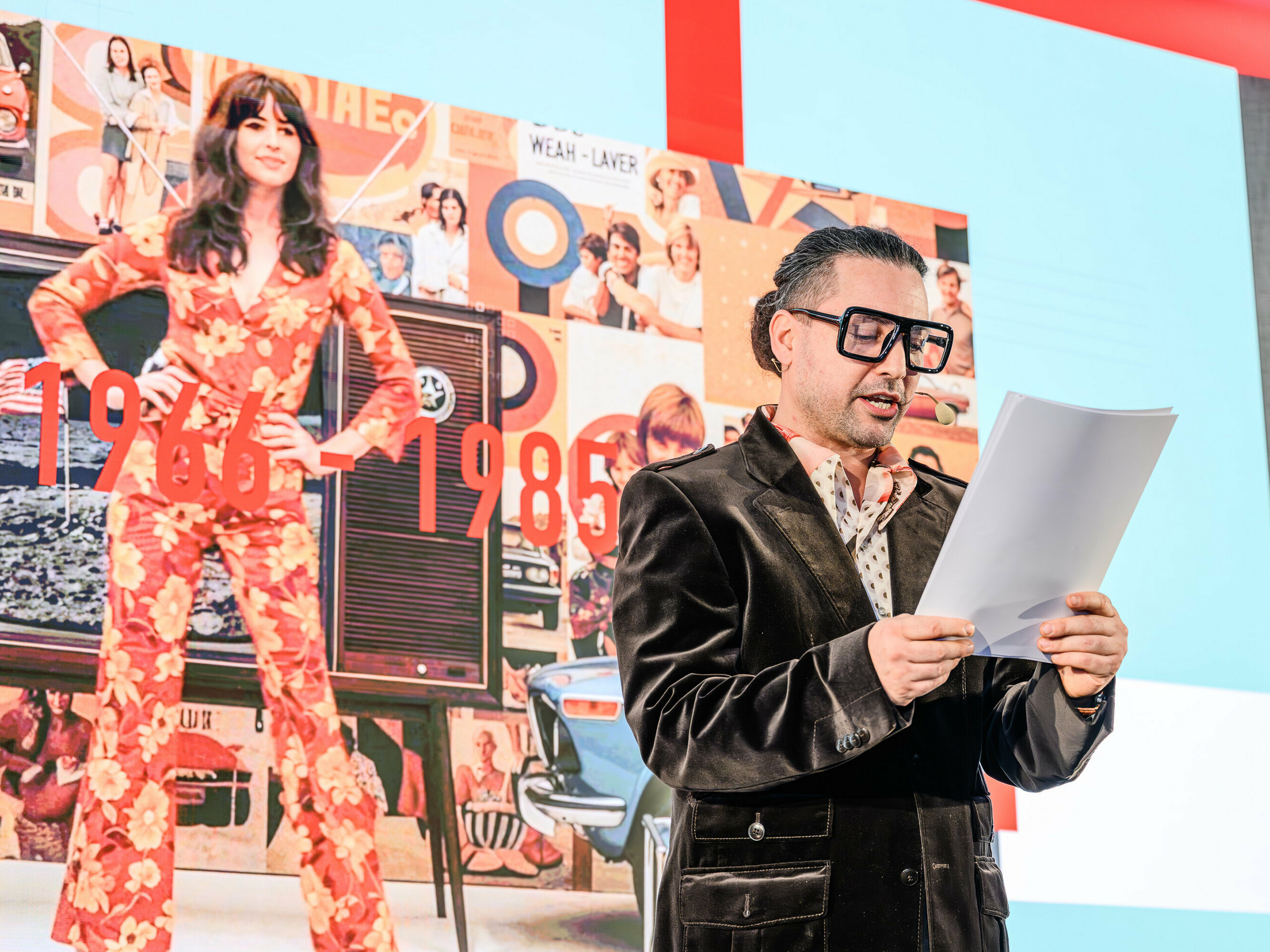 Potovanje skozi čas na odru predstavitve PREFARENZEN 2026: karizmatični Serkan Temel v retro stilu popelje občinstvo skozi desetletja. V središču pozornosti so leta od 1966 do 1985, ki so prikazana na kolažu v ozadju z ikonami oblikovanja in družbenimi trendi tistega časa. Tako kot izdelki PREFA tudi trendi preživijo s stilom in vsebino. Predstavitev kaže, kako arhitektura včerajšnjega dne postane navdih za rešitve jutrišnjega dne – na novo interpretirana z aluminijem.