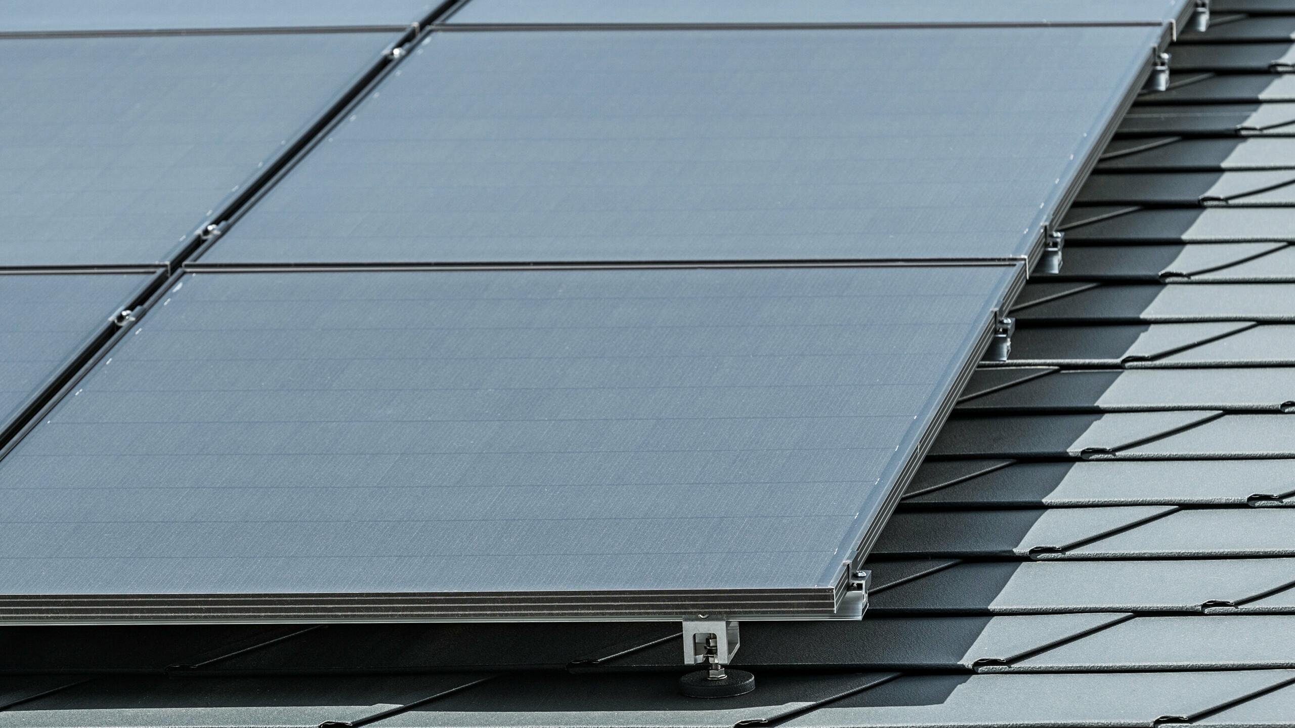 Bližnji posnetek fotonapetostnega sistema, nameščenega na strešnike PREFA DS.19 v antracitni barvi P.10 z nosilcem PREFA Solar Holder Vario