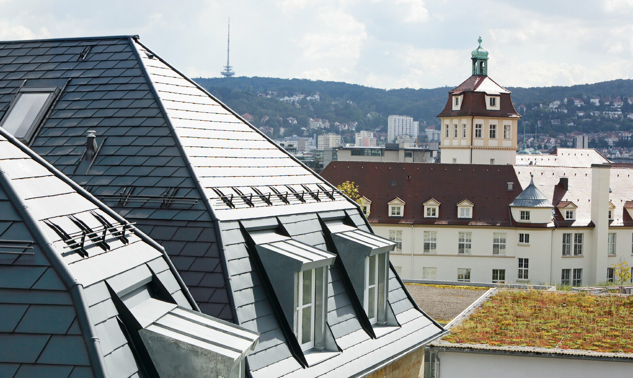 Stara meščanska hiša v Stuttgartu s pregibno streho in številnimi frčadnimi okni, prekrito z aluminijastimi strešnimi skodlami PREFA v barvi P.10 antracit