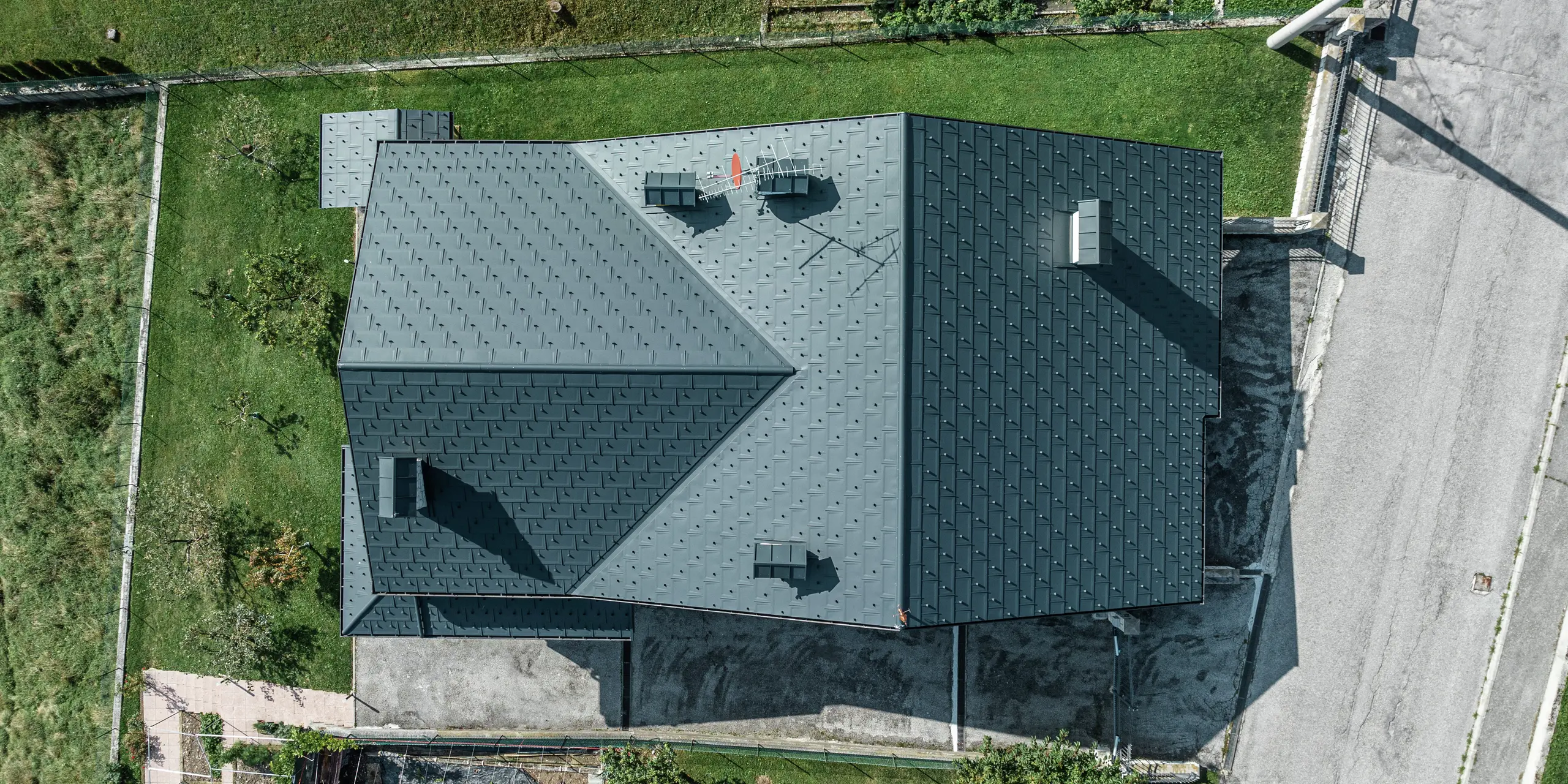 Drohnenaufnahme eines Einfamilienhauses in Gallio mit hochwertiger PREFA Dacheindeckung aus Dachplatten R.16 in P.10 Dunkelgrau. Die Aluminium-Dachlösung überzeugt durch moderne Optik, extreme Witterungsbeständigkeit und Langlebigkeit. Schneestopper sorgen für zusätzliche Sicherheit in alpinen Regionen. Die präzise Verarbeitung und das durchdachte Entwässerungssystem garantieren optimalen Schutz vor Regen und Schnee. Ein wartungsarmes Dach für Generationen.