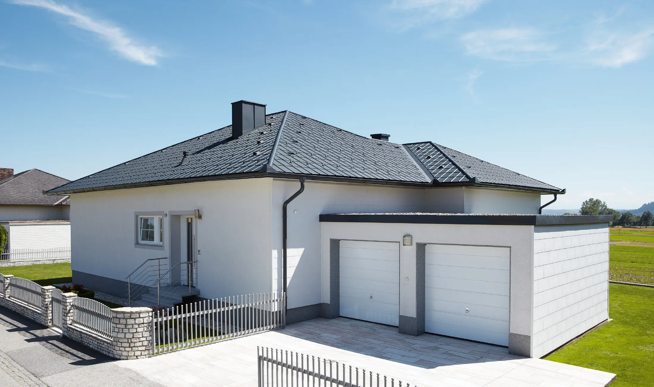 Novozgrajeni bungalov s šotorsko streho je bil prekrit s strešnimi ploščami PREFA v antracitni barvi P.10. Na desni strani je bila dodana dvojna garaža, fotografirana z ulice.
