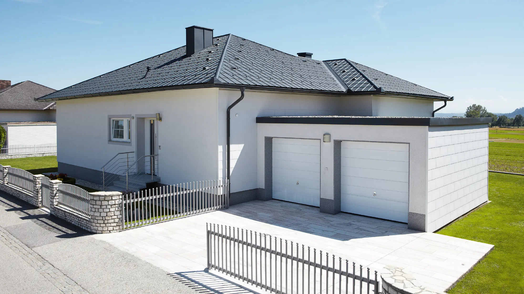 Novozgrajeni bungalov s šotorsko streho je bil prekrit s strešnimi ploščami PREFA v antracitni barvi P.10. Na desni strani je bila dodana dvojna garaža, fotografirana z ulice.