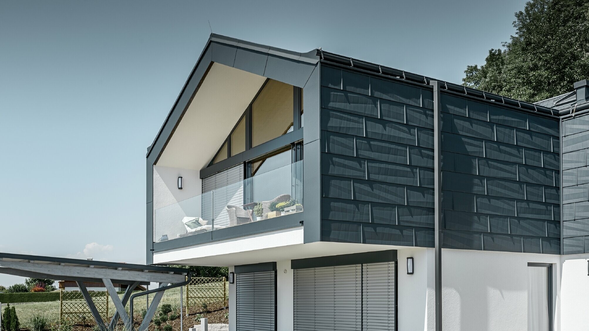 Sodobna večdružinska hiša z velikimi okni, streha in fasada sta oblečeni s strešnimi in fasadnimi paneli FX.12 antracitne barve