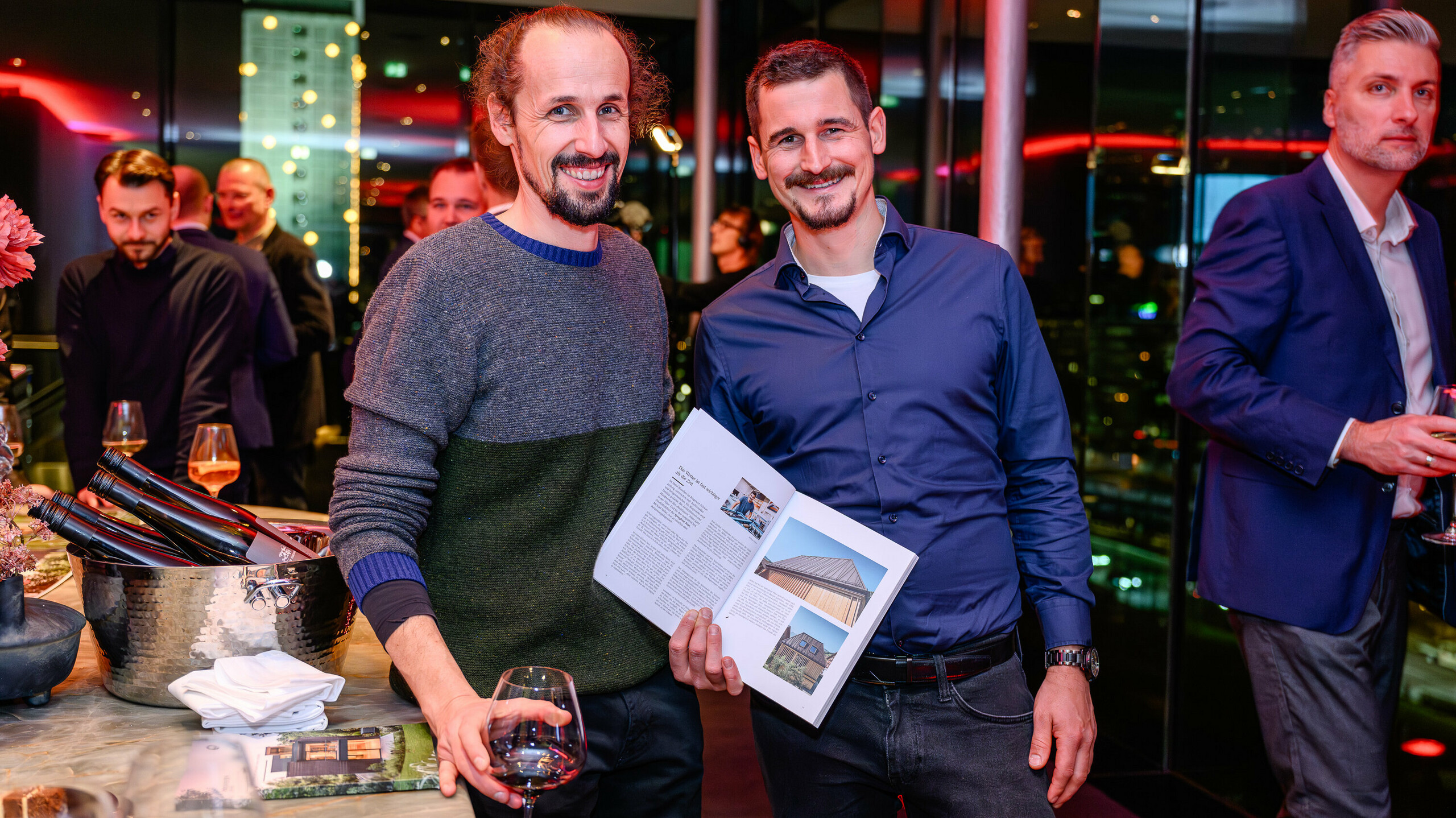 Žareči obrazi na predstavitvi PREFARENZEN 2026: dva udeleženca projekta ponosno predstavljata svoj objavljeni objekt v novi arhitekturni knjigi PREFA. Na sliki prikazana vila združuje naraven videz lesa s sistemom PREFALZ – odličen primer sodobnega kontrasta materialov in trajne estetike. Dogodek v k47.wien združuje oblikovanje, arhitekturo in mreženje na najvišji ravni. PREFA aluminijasti izdelki tu pokažejo svojo polno moč: so odporni na vremenske vplive, kreativno uporabni in oblikujejo stil za prihodnost usmerjene gradbene projekte. Večer poln ponosa, izmenjave in inovativnosti.