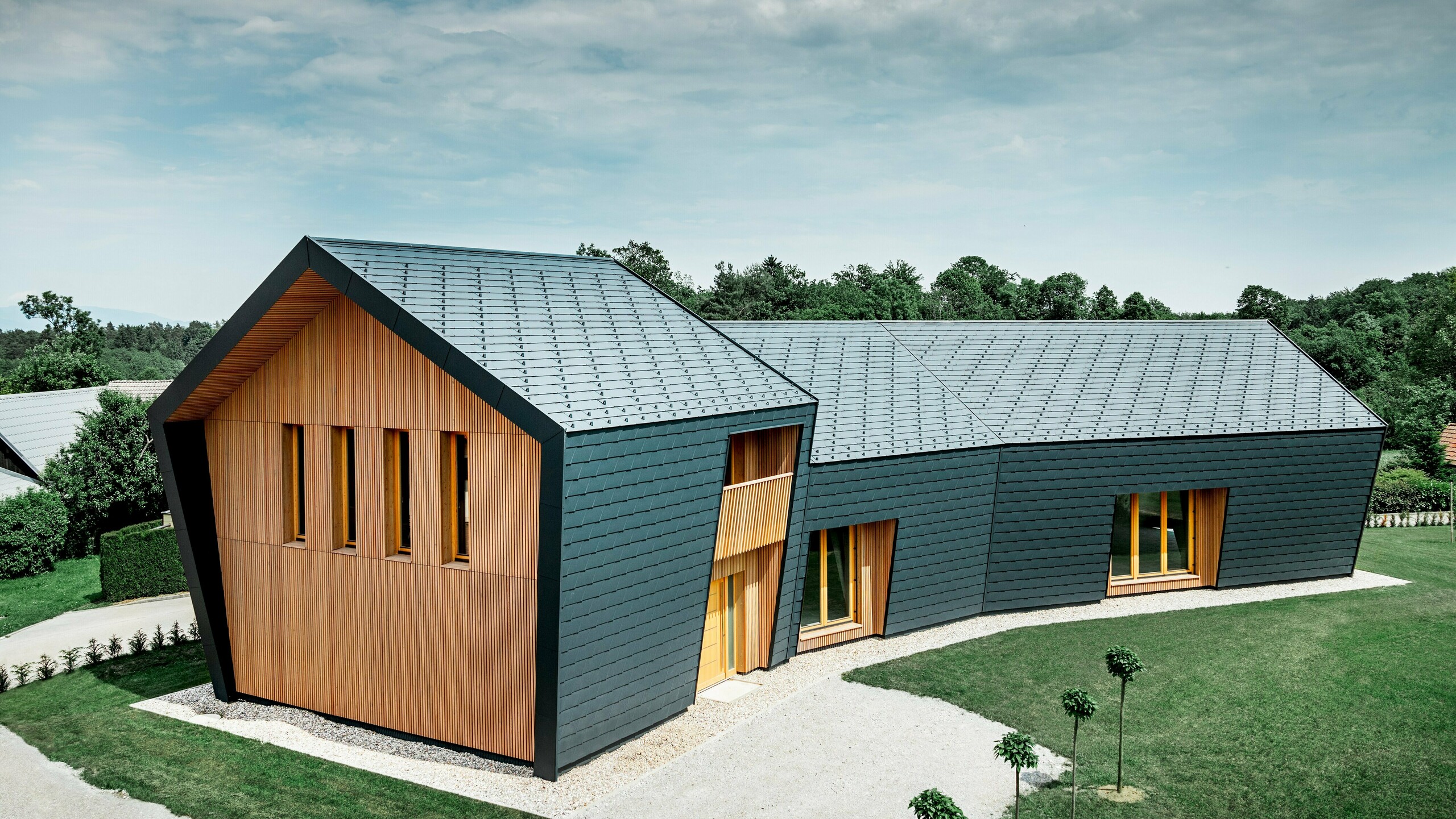 Gesamtansicht der Boulderhalle in Skofja; Die Kletterhalle ist am Dach und der seitlichen Fassade komplett mit der anthrazitfarbenen Schindel DS.19 von PREFA verkleidet. An der Stirnseite ist die Fassade mit hellem Lärchenholz verschalt.