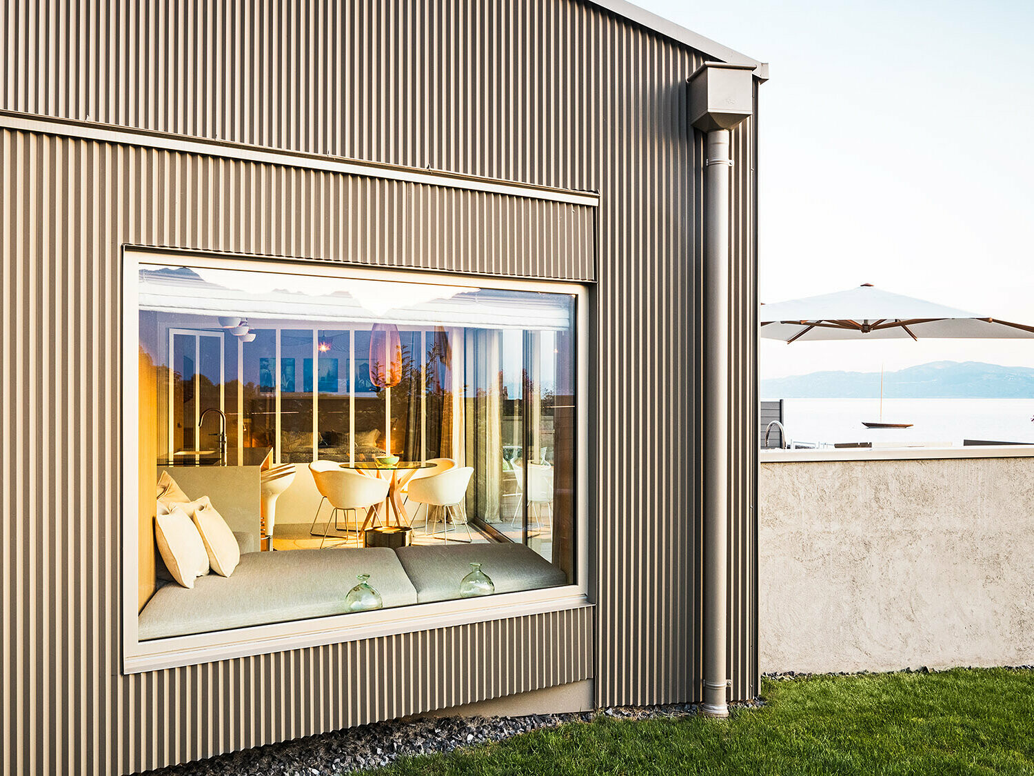 Stranski pogled na stavbo z nazobčano aluminijasto fasado, del osvetljene notranjosti je viden.