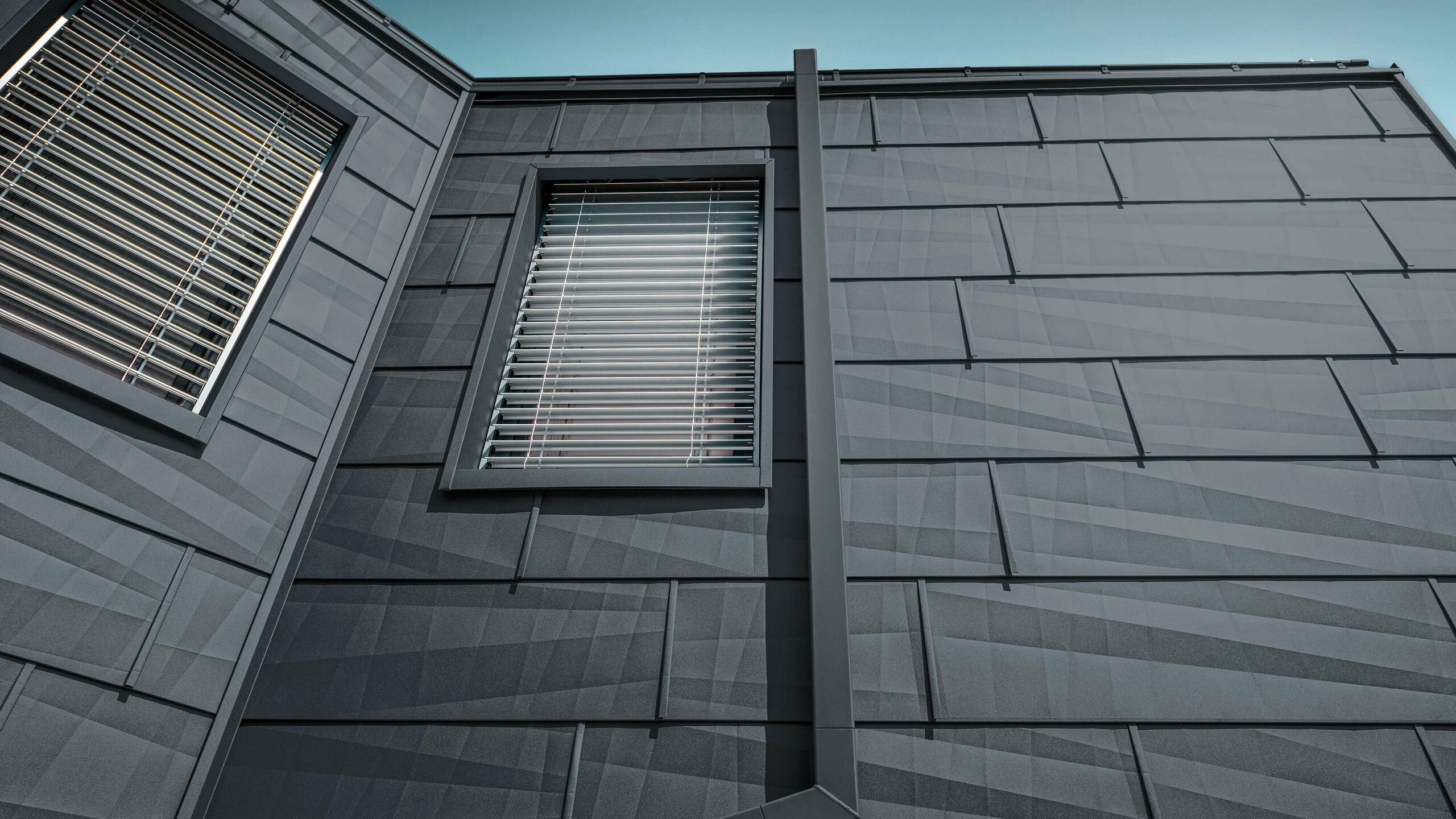 Fasada, obložena s fasadnim panelom FX.12 PREFA v antracitni barvi, aluminijasti paneli na fasadi z oglato odtočno cevjo, pravokotno iztočno cevjo, PREFA v antracitni barvi.