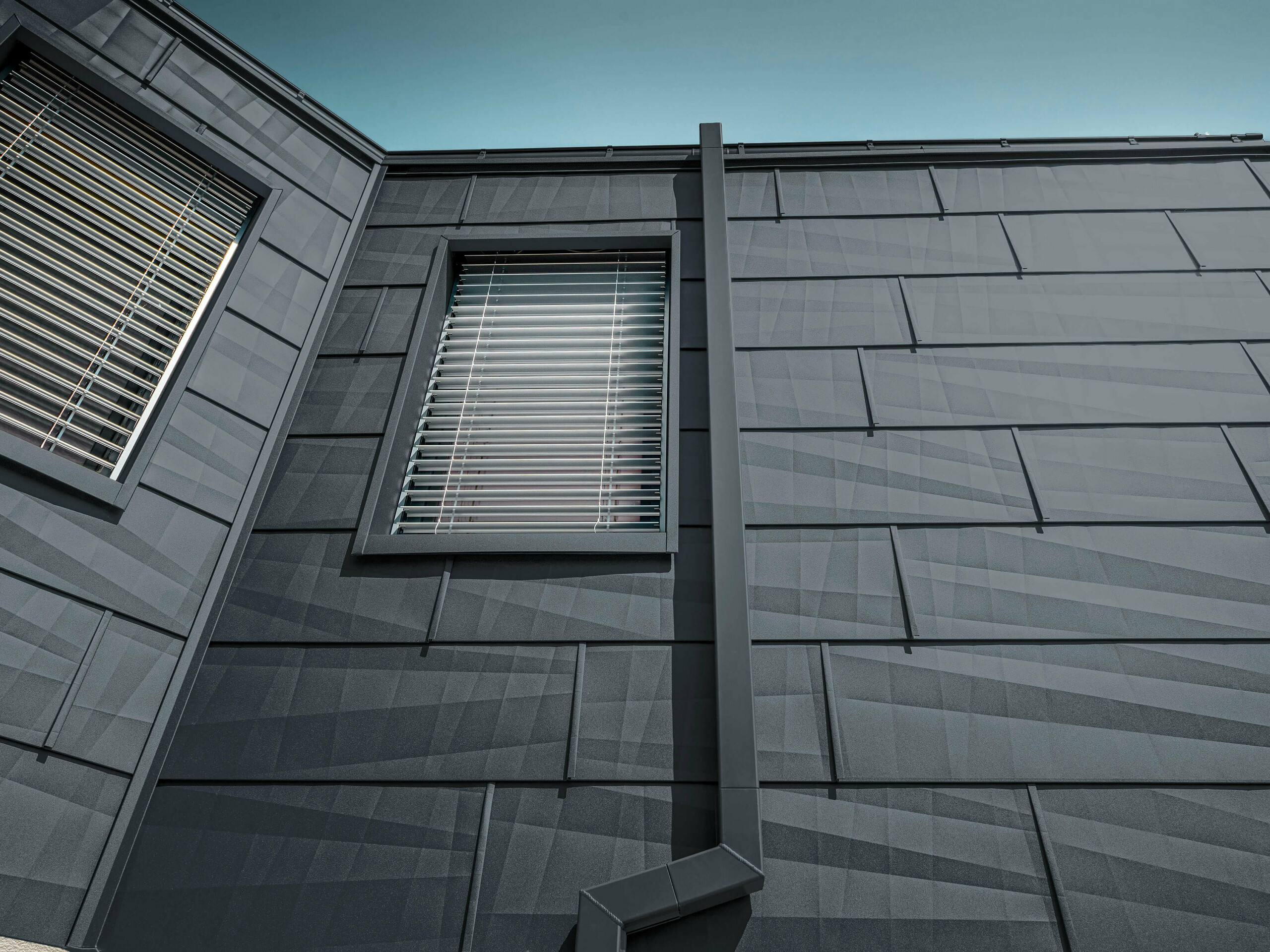 Fasada, obložena s fasadnim panelom FX.12 PREFA v antracitni barvi, aluminijasti paneli na fasadi z oglato odtočno cevjo, pravokotno iztočno cevjo, PREFA v antracitni barvi.