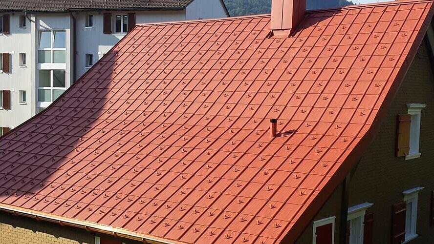 Dvokapna streha z aluminijasto streho PREFA. Streha v opečno rdeči barvi s snegolovi in dimnikom
