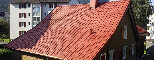 Dvokapna streha z aluminijasto streho PREFA. Streha v opečno rdeči barvi s snegolovi in dimnikom