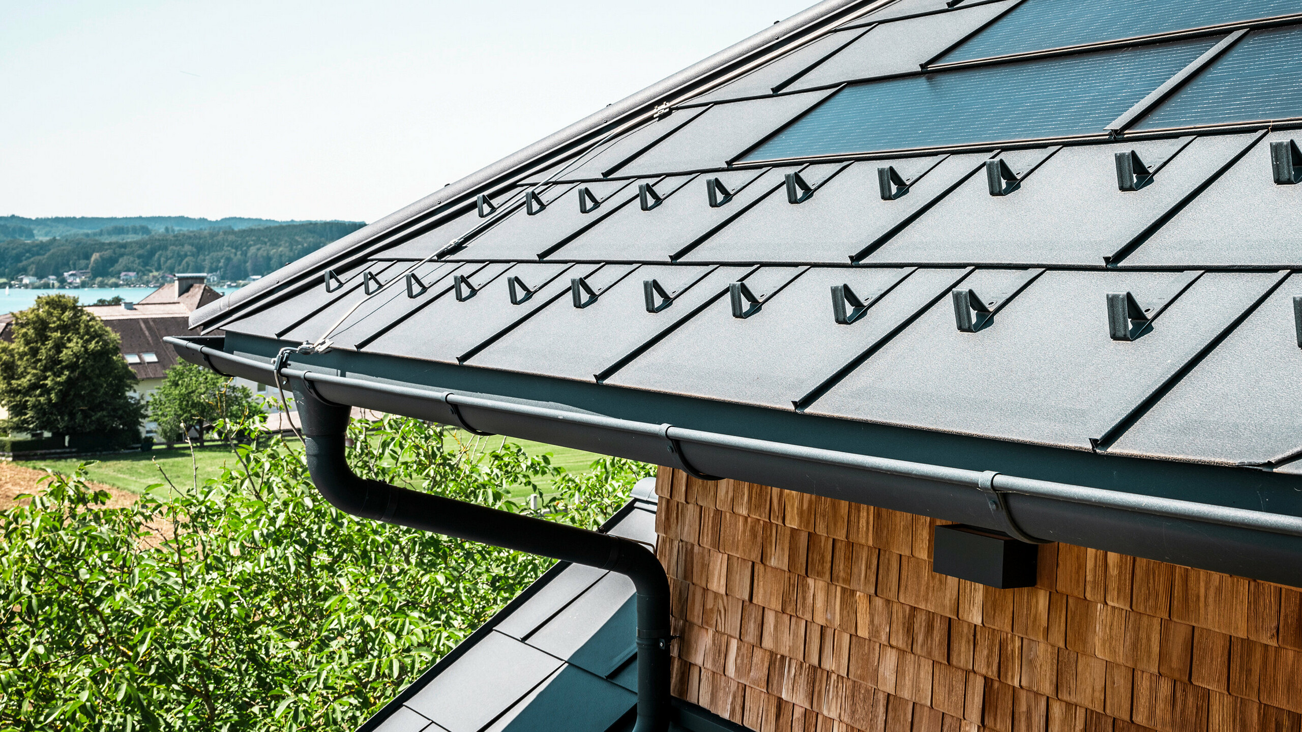 Gostilna Zenz'n Stub'n v Schörflingu ob jezeru Attersee se ponaša z novo obnovljeno streho z inovativnimi solarno strešnimi ploščami PREFA in trajnimi strešnimi ploščami PREFA R.16 v barvi P.10 antracitna. Elegantna aluminijasta streha združuje sodoben dizajn s trajnostno pridobivanjem energije. Tudi odvodnjavanje strehe, sestavljeno iz iztočne cevi in strešnega žleba v barvi P.10 antracitna, se harmonično vklaplja v celotno sliko in poudarja visoko kakovost izdelave. V ozadju se blešči modrina jezera Attersee.