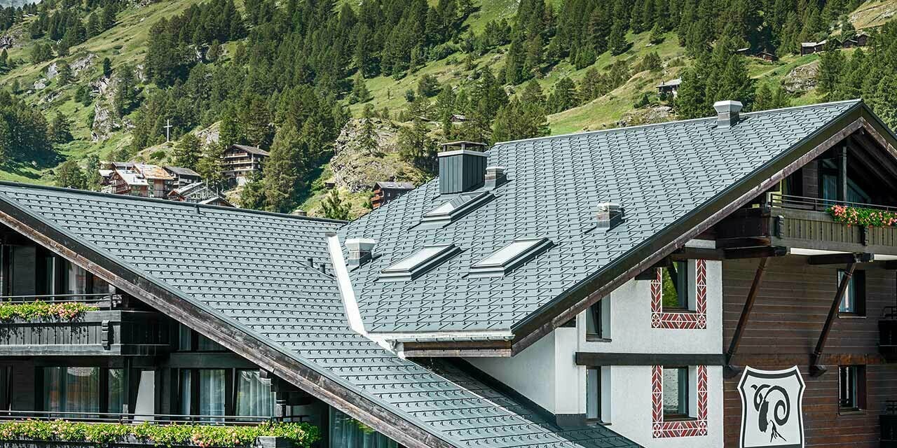 Hotel Alpenhof v Zermattu z Matterhornom v ozadju, z balkoni, temno leseno fasado in aluminijasto streho PREFA v antracitni barvi