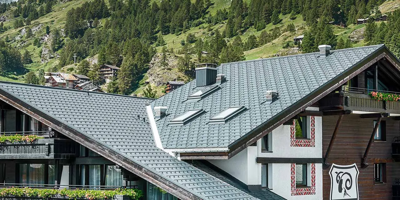Hotel Alpenhof v Zermattu z Matterhornom v ozadju, z balkoni, temno leseno fasado in aluminijasto streho PREFA v antracitni barvi