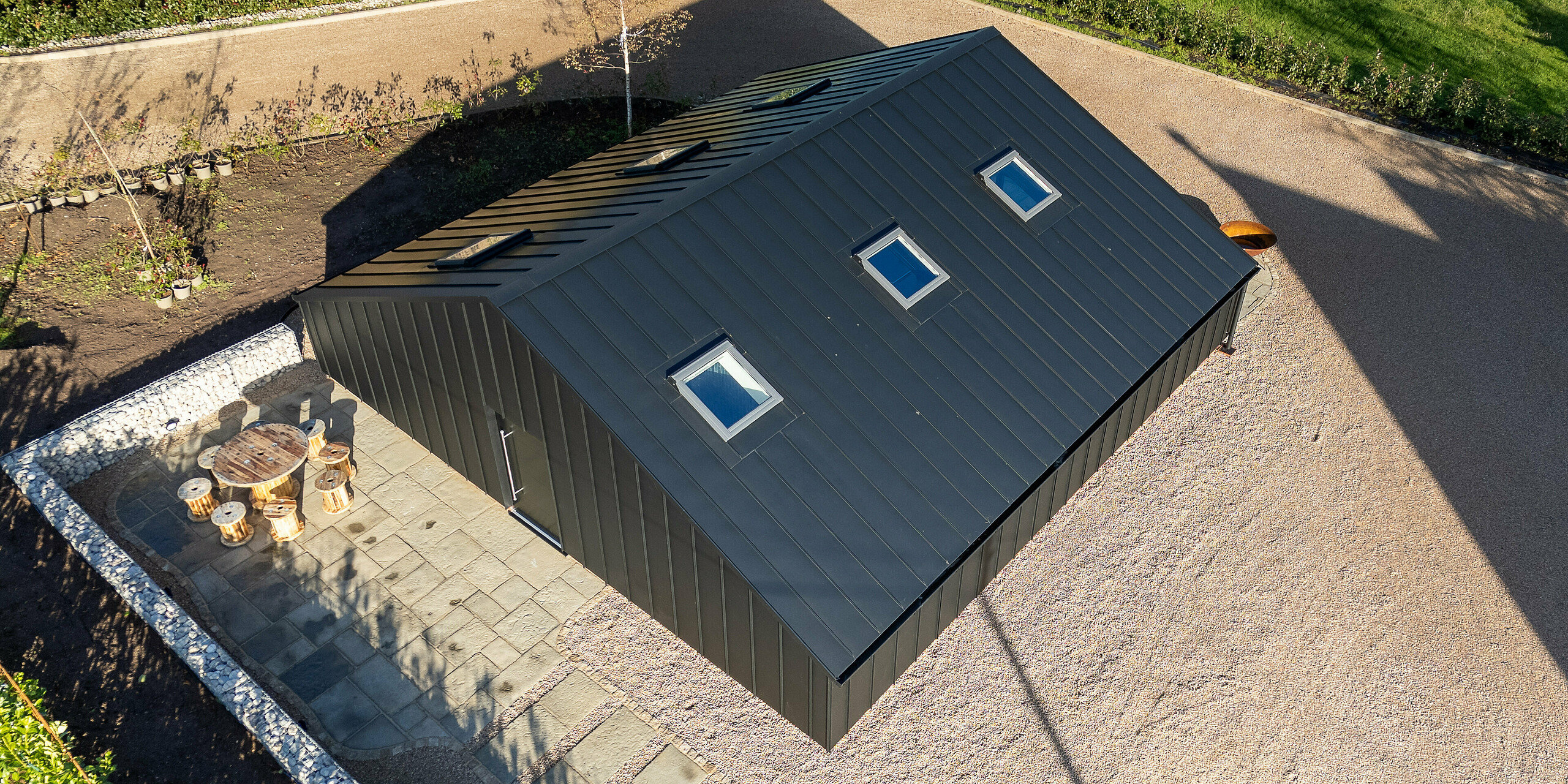 Draufsicht auf das moderne Freizeitgebäude in Ranton mit vollständig eingekleideter PREFA Aluminiumhülle in P.10 Schwarz. Das homogen ausgeführte PREFALZ Dach mit klaren Stehfalzlinien und integrierten Dachfenstern betont die elegante Architektur. Die robuste, witterungsbeständige Aluminiumoberfläche sorgt für dauerhafte Stabilität und setzt einen markanten Akzent im großzügigen Außenbereich.