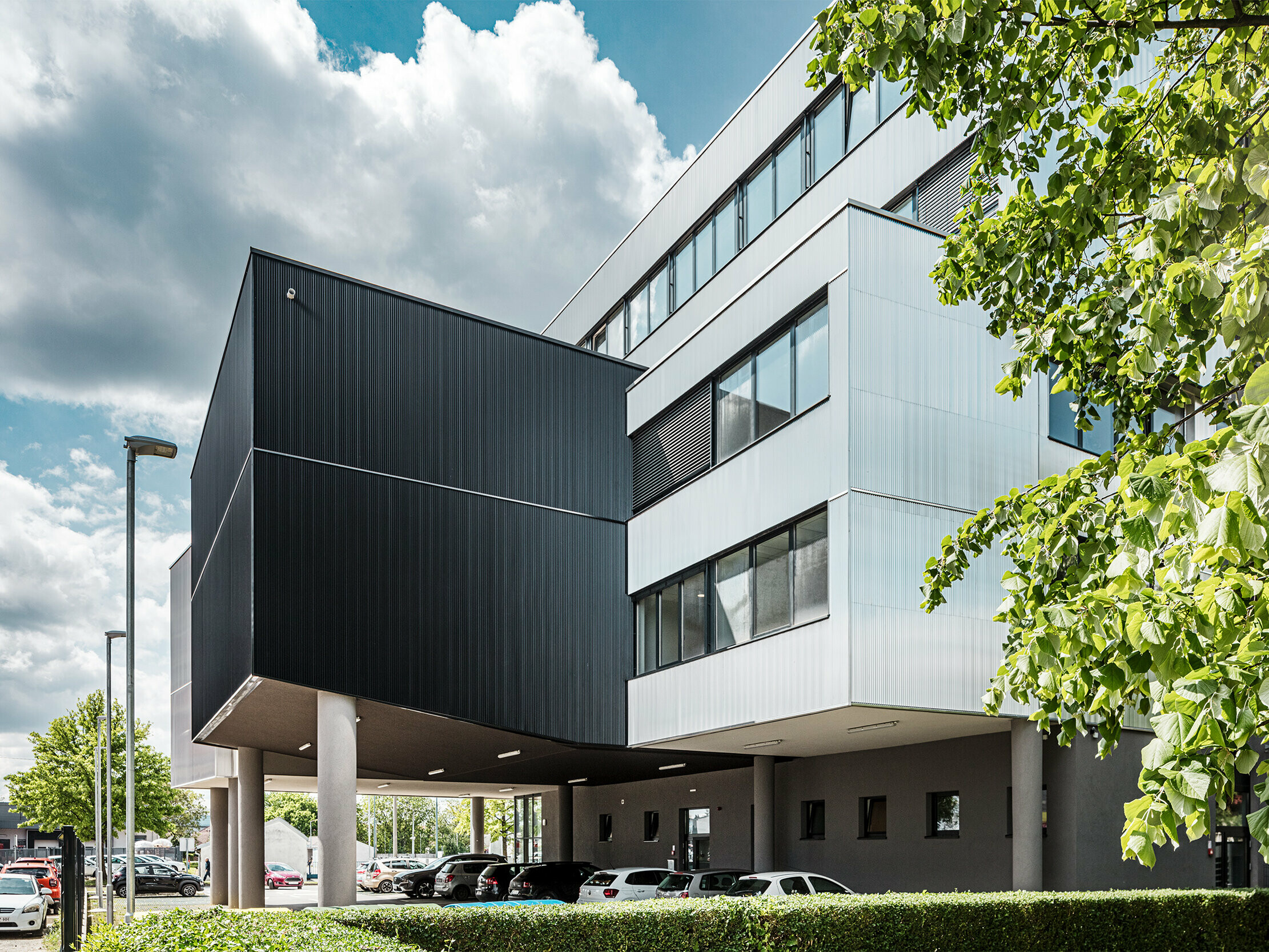 Sodobna poslovna stavba Glasbene šole Bjelovar na Hrvaškem se ponaša z izrazito aluminijasto fasado iz PREFA ekstrudirano stikanih zobčastih profilov. Črno in srebrno eloksirane fasadne površine ustvarjajo jasne arhitekturne kontraste ter stavbi dajejo značaj in globino. Navpično vgrajeni profili oblikujejo elegantno strukturo z dinamično igro svetlobe in senc. Zaradi robustne, proti koroziji odporne aluminijaste površine so fasadni elementi izjemno trajni in nezahtevni za vzdrževanje. Skrita pritrditev zagotavlja enakomeren in kakovosten videz. Ta obešena, prezračevana PREFA fasada združuje oblikovanje, tehniko in funkcionalnost.