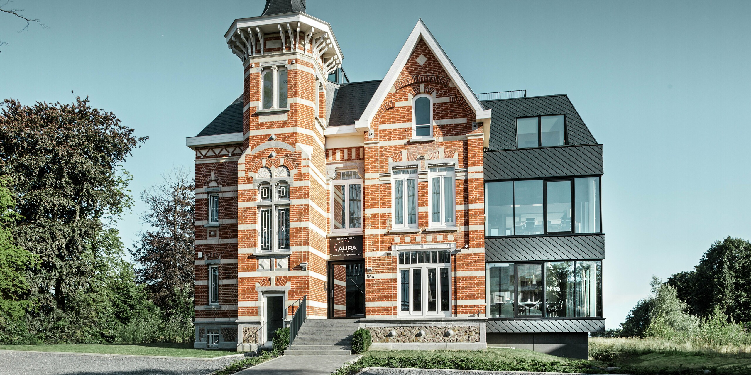 Historisches Backsteinschlösschen Kasteeltje Heizel mit markantem Turm trifft auf modernen Zubau aus Glas und anthrazitfarbenen PREFA Wandrauten. Die kontrastreiche Fassade verbindet Tradition und Innovation, während die klare Linienführung und großen Fensterflächen Offenheit und Leichtigkeit ausstrahlen. Ein spannender Eyecatcher, der Langlebigkeit, Design und Nachhaltigkeit architektonisch vereint.
