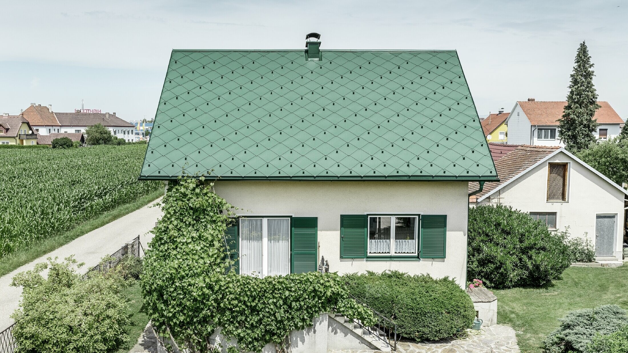 Klasična enodružinska hiša z dvokapno streho s strešno kritino iz aluminija PREFA v mahovo zeleni barvi z zelenimi polkni. Streha je bila izdelana s strešnimi rombi 44 × 44 PREFA v barvi P.10 mahovo zelena.