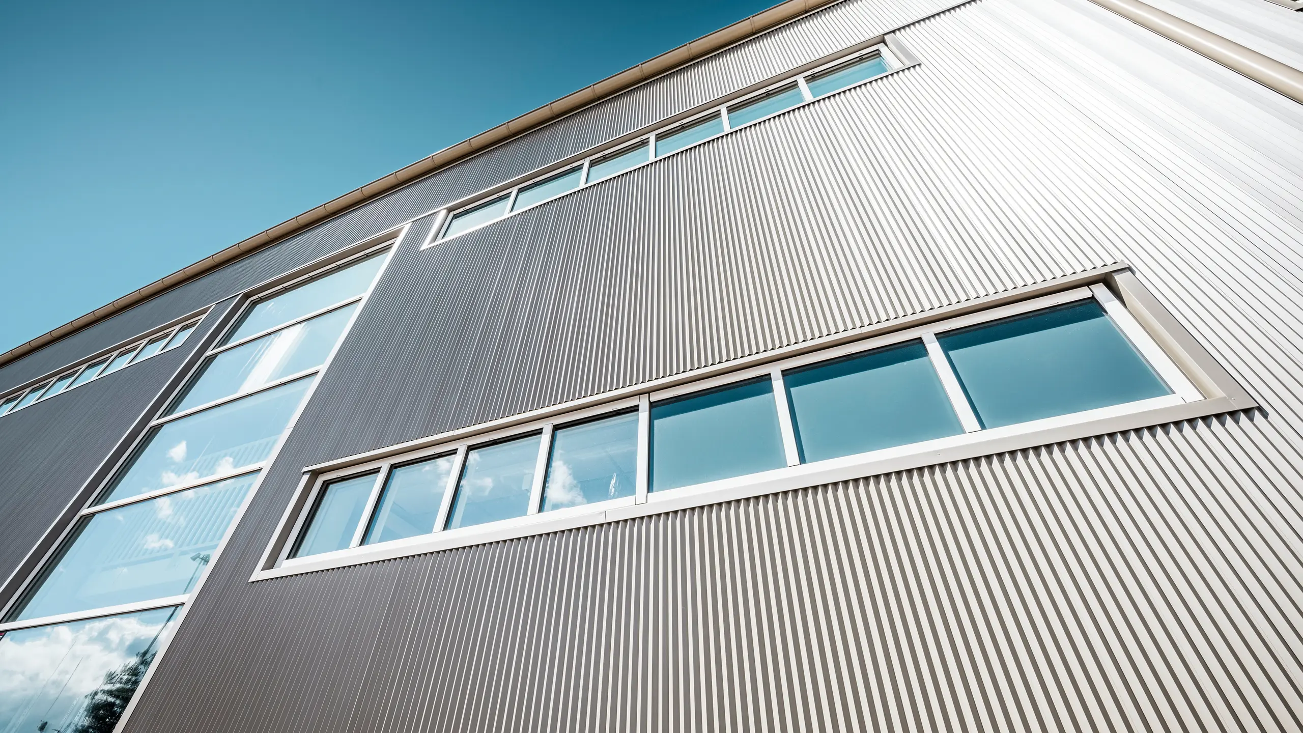 Außenansicht der Park Arena in Värnamo, Schweden, mit einer modernen PREFA Fassade in Bronze. Die Zackenprofile aus Aluminium schaffen markante Licht- und Schatteneffekte. Die eingebetteten Fenster fügen sich harmonisch in die präzise verarbeitete Fassade ein, die für Langlebigkeit, Widerstandsfähigkeit und zeitgemäßes Design steht.