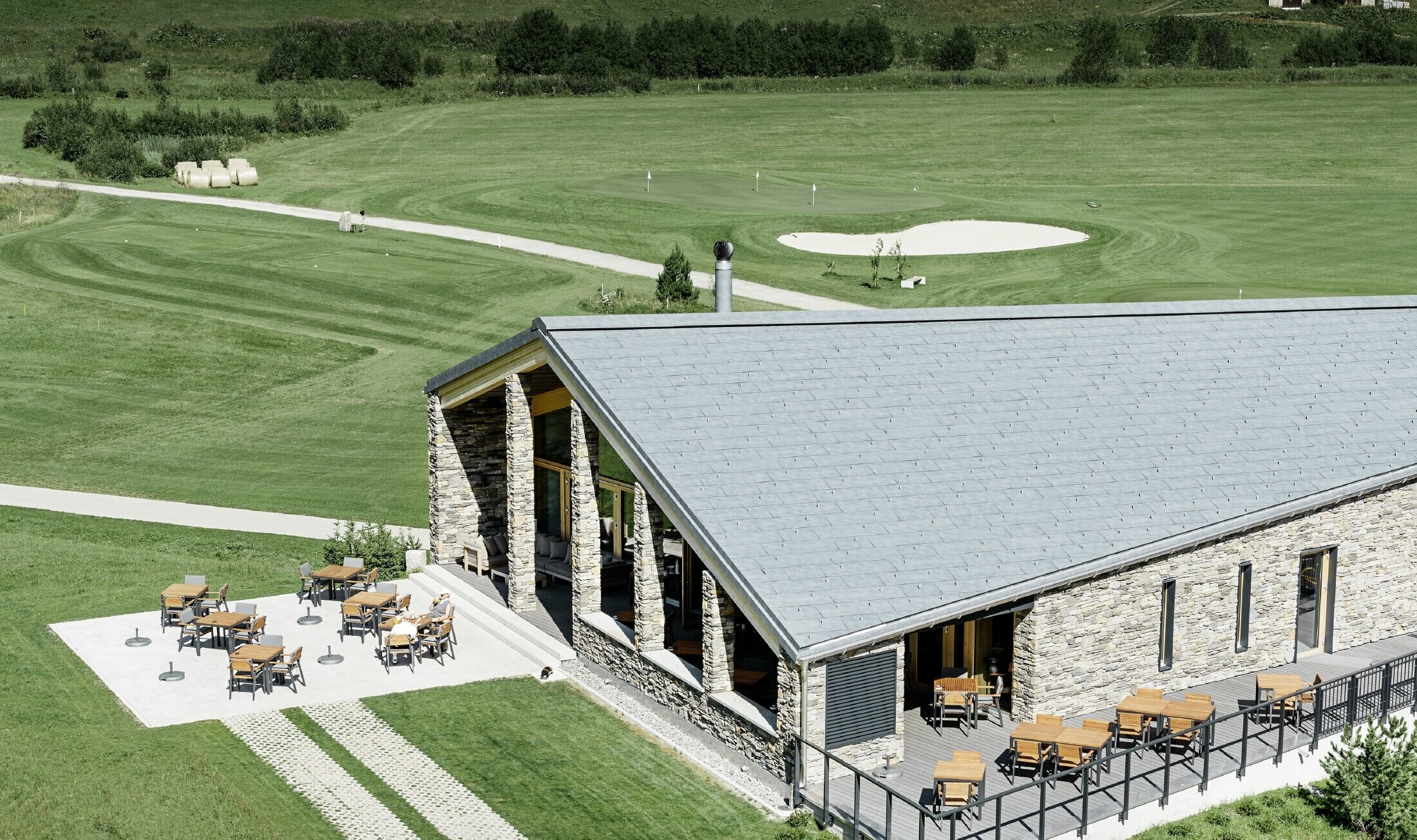 Sodobna klubska hišica golf igrišča v Andermattu s kamnito fasado in strešnimi paneli PREFA FX.12 iz aluminija v kamnito sivi barvi