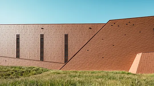 Črpalna postaja za pitno vodo v Lottumu (Nizozemska) se kot skulpturalna arhitekturna masa harmonično uvršča v naravno okolje. Izrazita aluminijasta fasada PREFA Siding.X v topli rjavi barvi tvori zanimiv kontrast z zelenim travnikom in griči ter navdušuje s svojo fino strukturirano, živo površino. Tanke, navpične odprtine ustvarjajo natančne poudarke. Trajni, lahki in v celoti reciklirani PREFA aluminijasti paneli prepričajo z visoko odpornostjo proti vremenskim vplivom, barvno obstojnostjo ter trajnostno, vzdrževanju prijazno ovojnico stavbe. S tem je črpalnica pitne vode arhitekturni magnet za poglede v infrastrukturni gradnji.