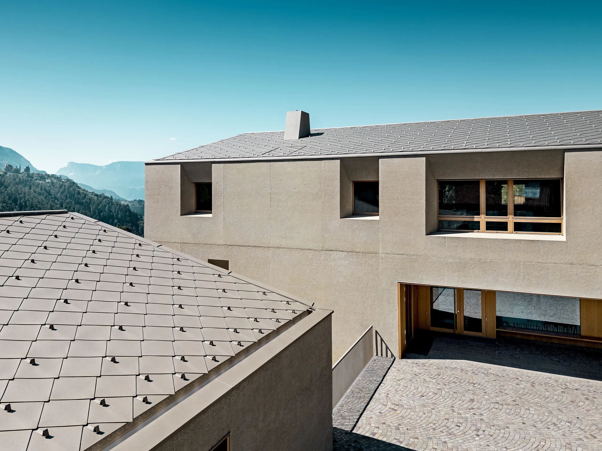 Detajlni pogled na izobraževalni center Riffian s strešnimi rombi PREFA 44 × 44 v barvi P.10 bronasta. Natančno izvedena aluminijasta strešna kritina na stavbah s čistimi arhitekturnimi linijami poudarja sodobno arhitekturo, zagotavlja dolgotrajno zaščito pred vremenskimi vplivi ter se harmonično zliva z naravno gorsko pokrajino Južne Tirolske.