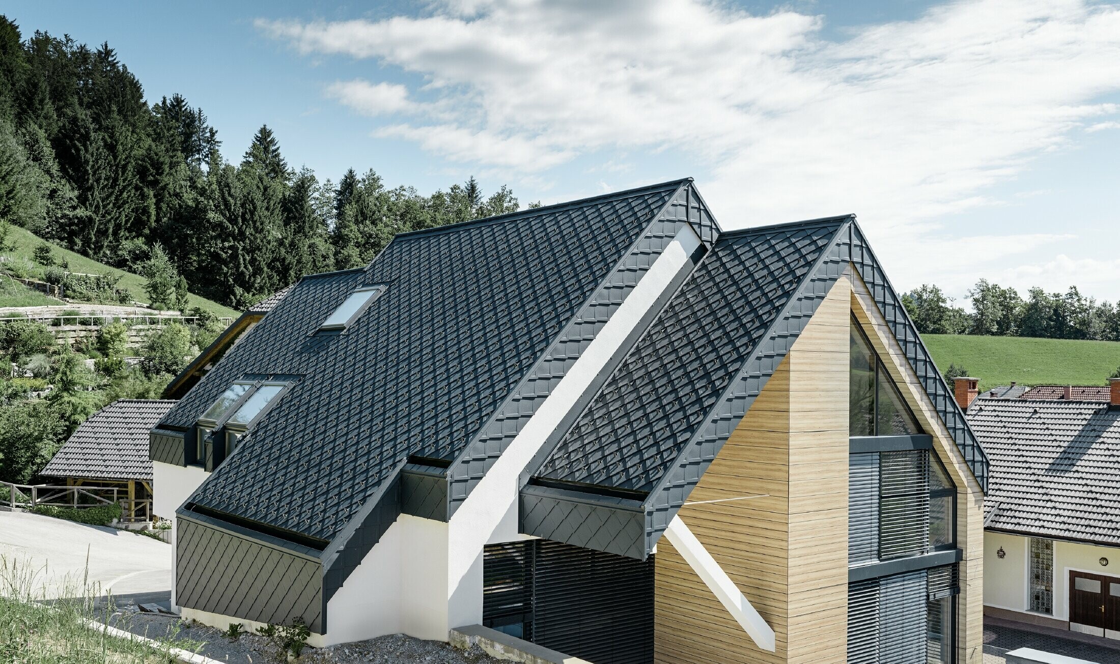 Enodružinska hiša z dvokapno streho brez strešnega napušča s fasado v videzu lesa in aluminijasto streho v antracitni barvi.