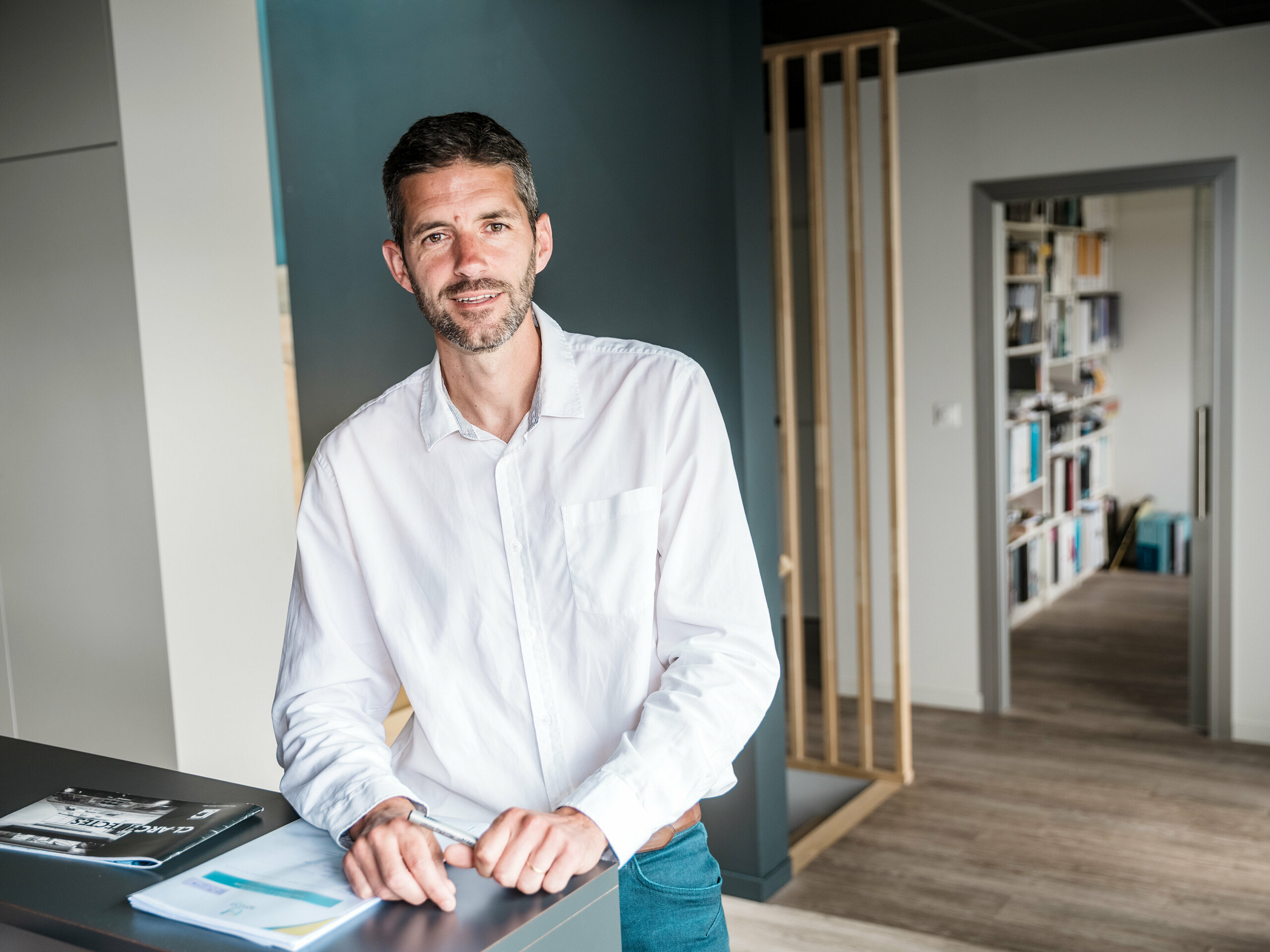 V ospredju slike je arhitekt Hugues Launay iz arhitekturnega biroja CLARC Architectes. Moški je postavljen v sredini oziroma nekoliko levo in nosi formalna oblačila, primerna za profesionalni intervju. V ozadju je vidna ukrivljena aluminijasta fasada Collège Léontine Dolivet, katere kovinsko srebrna površina ustvarja svetlobne odseve. Oseba gleda rahlo vstran, njena drža je samozavestna in odločna, kar nakazuje, da je odgovorna za projekt. Slika je posneta pri dnevni svetlobi, z mehko, naravno svetlobo, ki jasno poudarja konture.