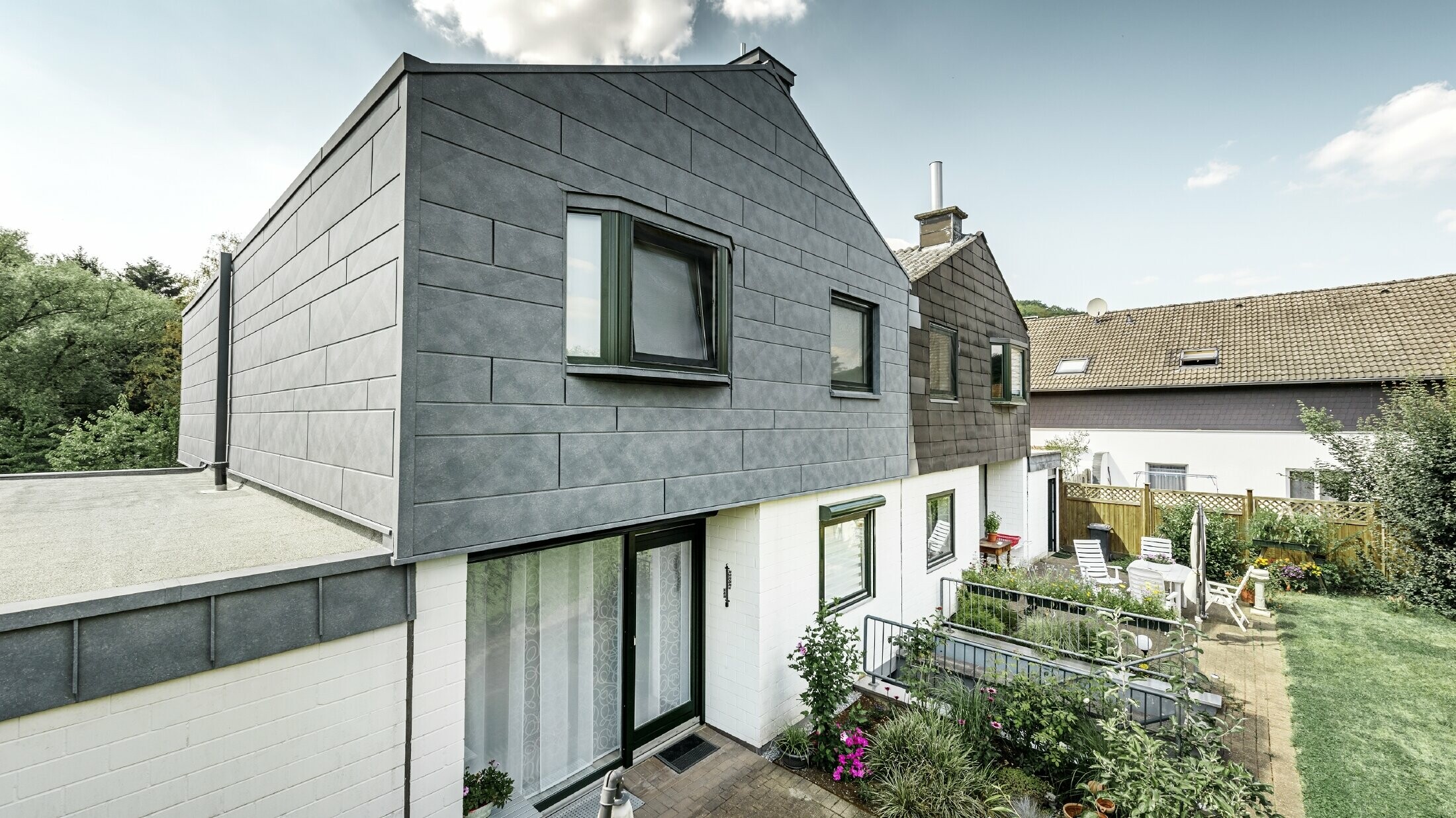 Zgornji del dvojne hiše je bil obnovljen s PREFA fasadnim elementom Siding.X v barvi P.10 kamnito siva. Za primerjavo je takoj zraven polovica hiše pred obnovo.