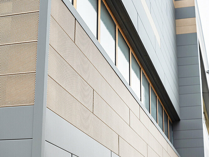 Elementi za fasado PREFA Siding so zdaj na voljo tudi v perforirani, torej luknjani izvedbi, pri čemer so peščeno rjavi luknjani elementi kombinirani s sivimi paneli. 