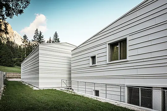 Zadnja stran vojašnice Tempesti v Corvari ponuja slikovito perspektivo: videti so gozdna drevesa, jasno modro nebo in gore, ki jih osvetljuje sonce. Svetla aluminijasta fasada s svojo jasno strukturo kaže tehnično izpopolnjenost PREFALZA v barvi P.10 prefa bela. Horizontalni aluminijasti trakovi odbijajo svetlobo, nudijo optimalno zaščito pred vremenskimi vplivi in se harmonično zlijejo z alpskim okoljem. Odličen primer trajne in moderne vojaške arhitekture!