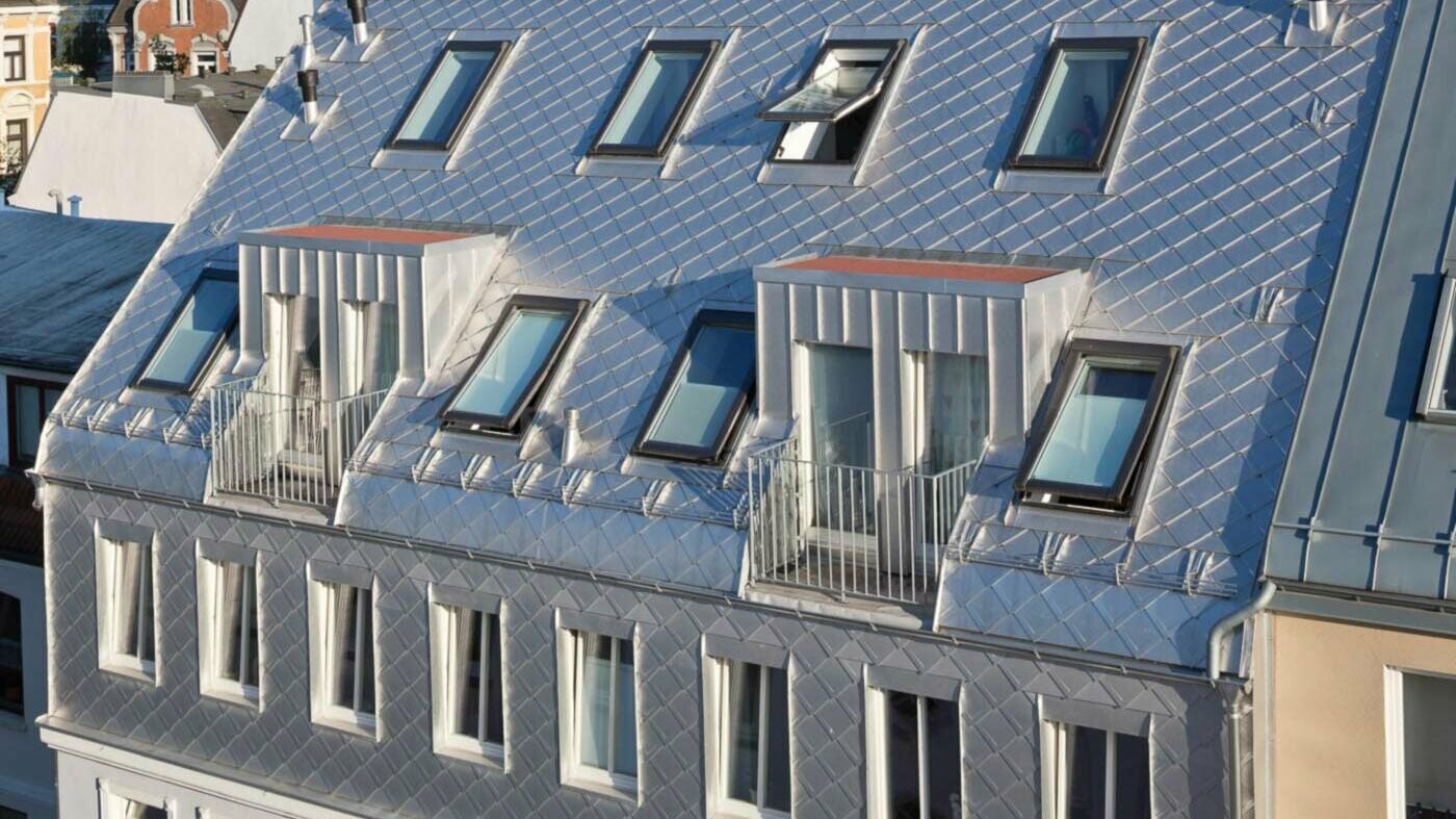 Izvedba mansarde s številnimi strešnimi okni in aluminijasto streho v naravni aluminijasti barvi z elementi v videzu lusk