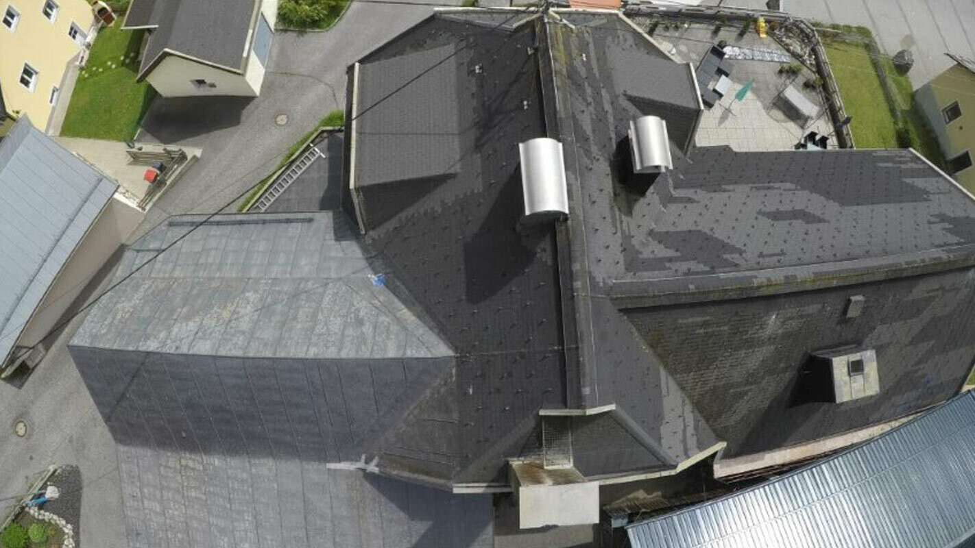 Ptičja perspektiva stare strehe s številnimi podrobnostmi – žlotami, mansardnimi okni in dimniki. Stara strešna kritina je bila že večkrat popravljena in je polna madežev.