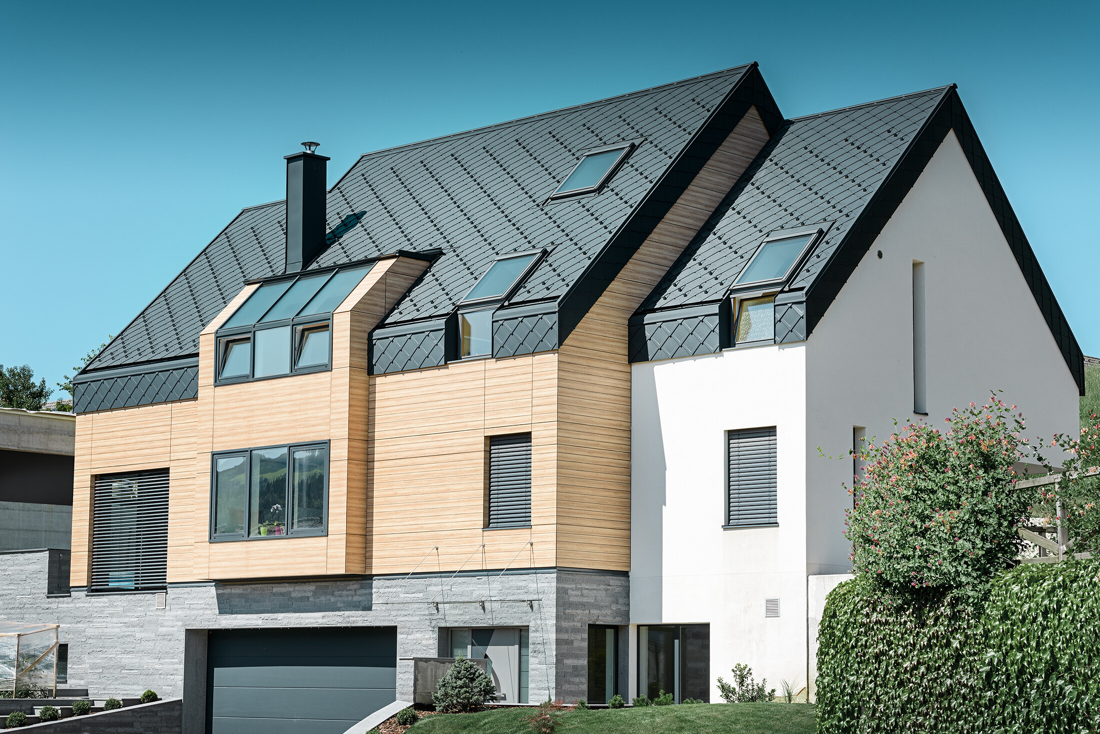 Sodobna novogradnja, pri kateri strešna kritina sega tudi prek zgornjega dela fasade, za kritino so uporabljeni aluminijasti strešni rombi v antracitni barvi.