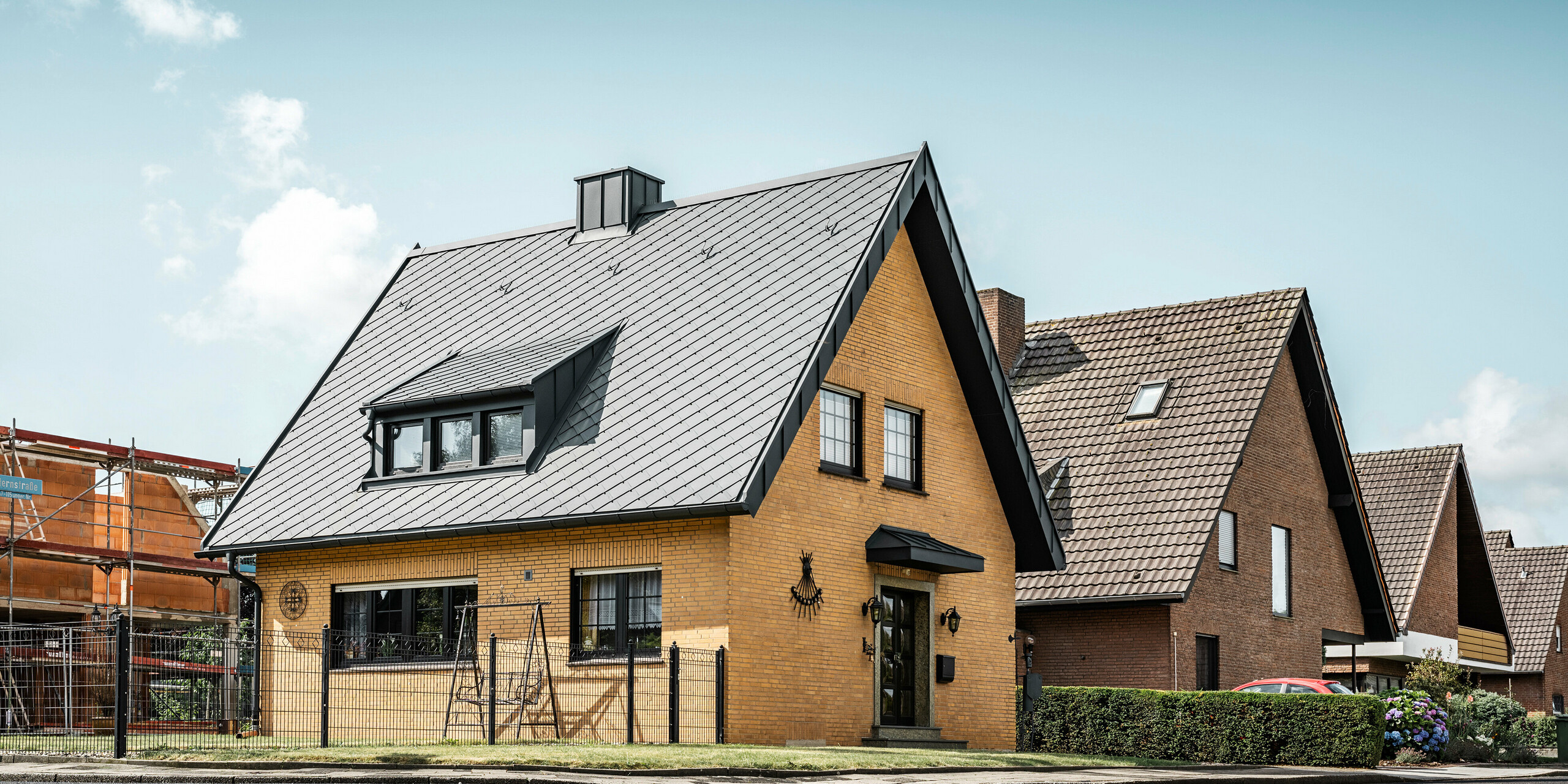 Tradicionalna rumena opečnata hiša v Tönisvorstu s koničasto dvokapno streho, prekrito s PREFA strešnimi rombi 29×29 v antracitni barvi. Mansardno okno in dimnik, prav tako v antracitni barvi, se prilegata strehi. Podobno videz zaokrožita žleb in odtočna cev. Hiša stoji v stanovanjskem naselju, obdanem s podobnimi stavbami, s svojo streho pa doda sodoben pridih.