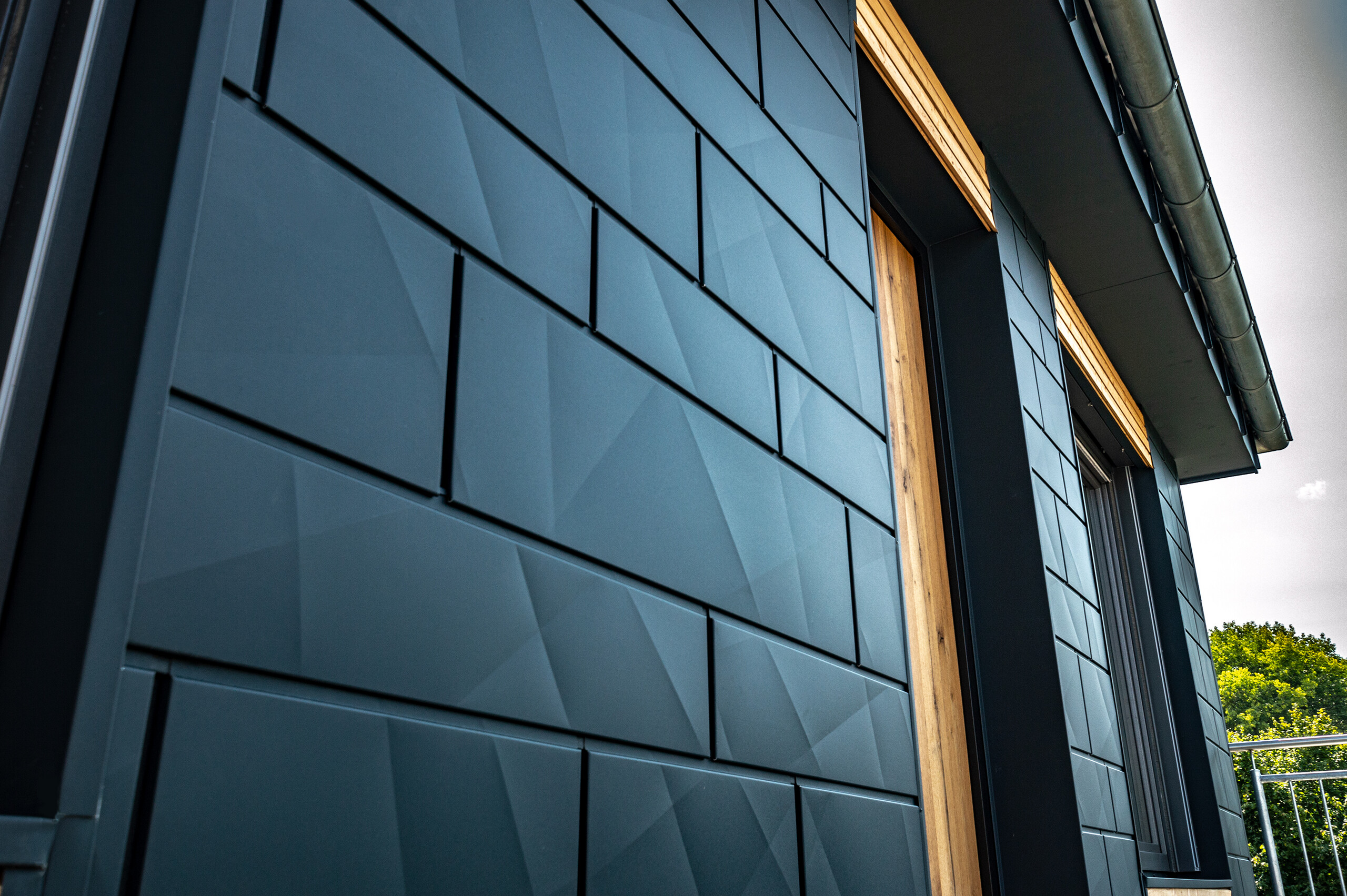 Fasada s PREFA Siding.X v antracitni barvi, kombinirana z balkonskimi vrati in velikimi steklenimi površinami ter lesenimi fasadnimi oblogami.