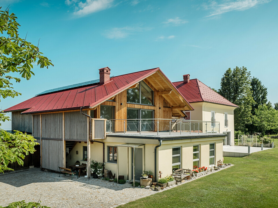 Die beiden sanierten Einfamilienhäuser in Aschach an der Steyr beeindrucken durch ihre harmonische Dachgestaltung. Die PREFA Dachraute 44 x 44 in der Farbe P.10 Oxydrot verleiht ihnen ein markantes, zeitloses Aussehen und bildet einen starken Kontrast zur modernen Holzverkleidung bzw. der gelblichen Putzfassade. Hervorzuheben sind zudem die großflächigen Fenster, welche die Offenheit des Obergeschosses noch verstärken. Das großzügige Grundstück und die gepflegte Gartenlandschaft betonen die gelungene Verbindung von Natur, Tradition und Moderne. Die PREFA Dachrauten sind nicht nur ästhetisch ansprechend, sondern auch äußerst beständig und langlebig – ideal für jedes Wetter.