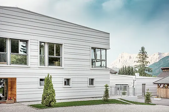 Podrobni pogled na vojašnico „Tempesti“ s precizno položenimi trakovi PREFALZ v barvi P.10 prefa bela. Jasne linije vodoravno položenih trakov poudarjajo moderno oblikovanje fasade. Svetla površina odbija sončno svetlobo in optimizira mikroklimo. V ozadju se dvigajo impresivne južnotirolske gore – tu se tehnologija sreča z naravo na najvišji ravni.