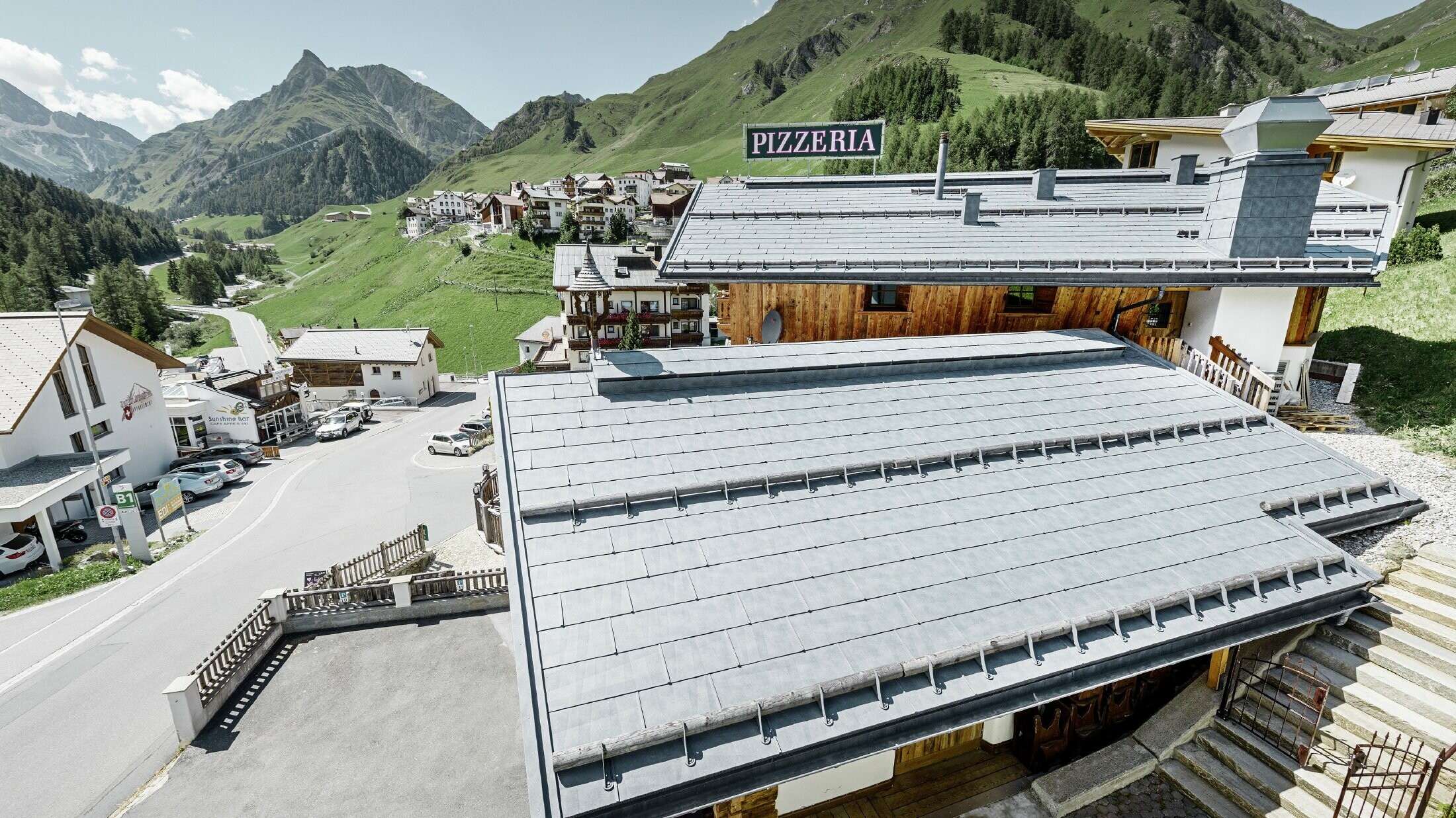 Restavracija Almrausch s hribi v ozadju in streho PREFA s strešnimi paneli FX.12 v kamnito sivi barvi ter snegolovi