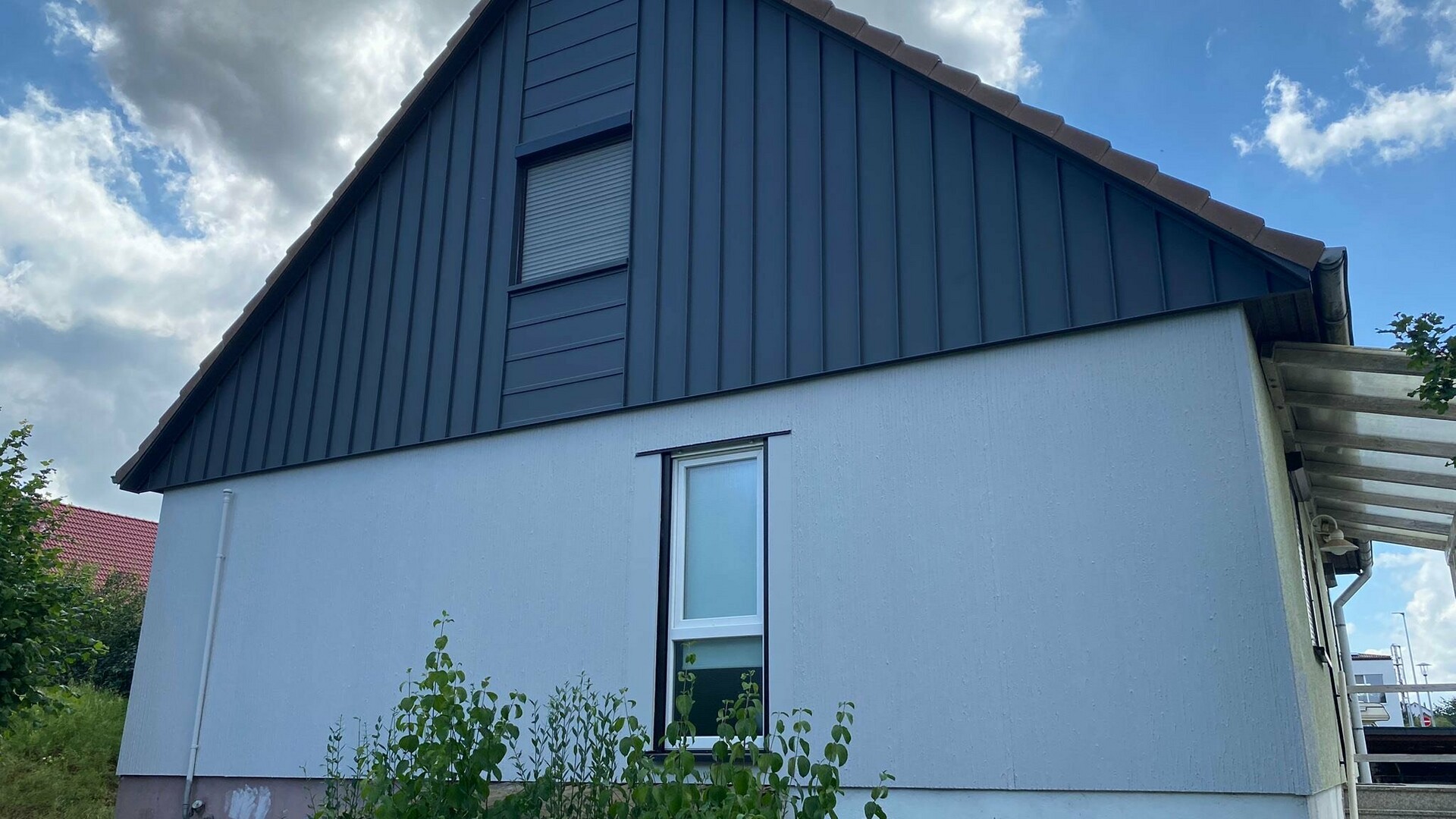 Ein Einfamilienhaus nach der Sanierung mit einer modernen Aluminiumfassade von PREFA. Die robuste Winkelstehfalzfassade in Kombination mit einer abgesetzten Liegefalzfassade in PREFALZ P.10 Dunkelgrau sorgt für eine langlebige, witterungsbeständige Ausführung und verleiht dem Gebäude eine zeitgemäße Optik.