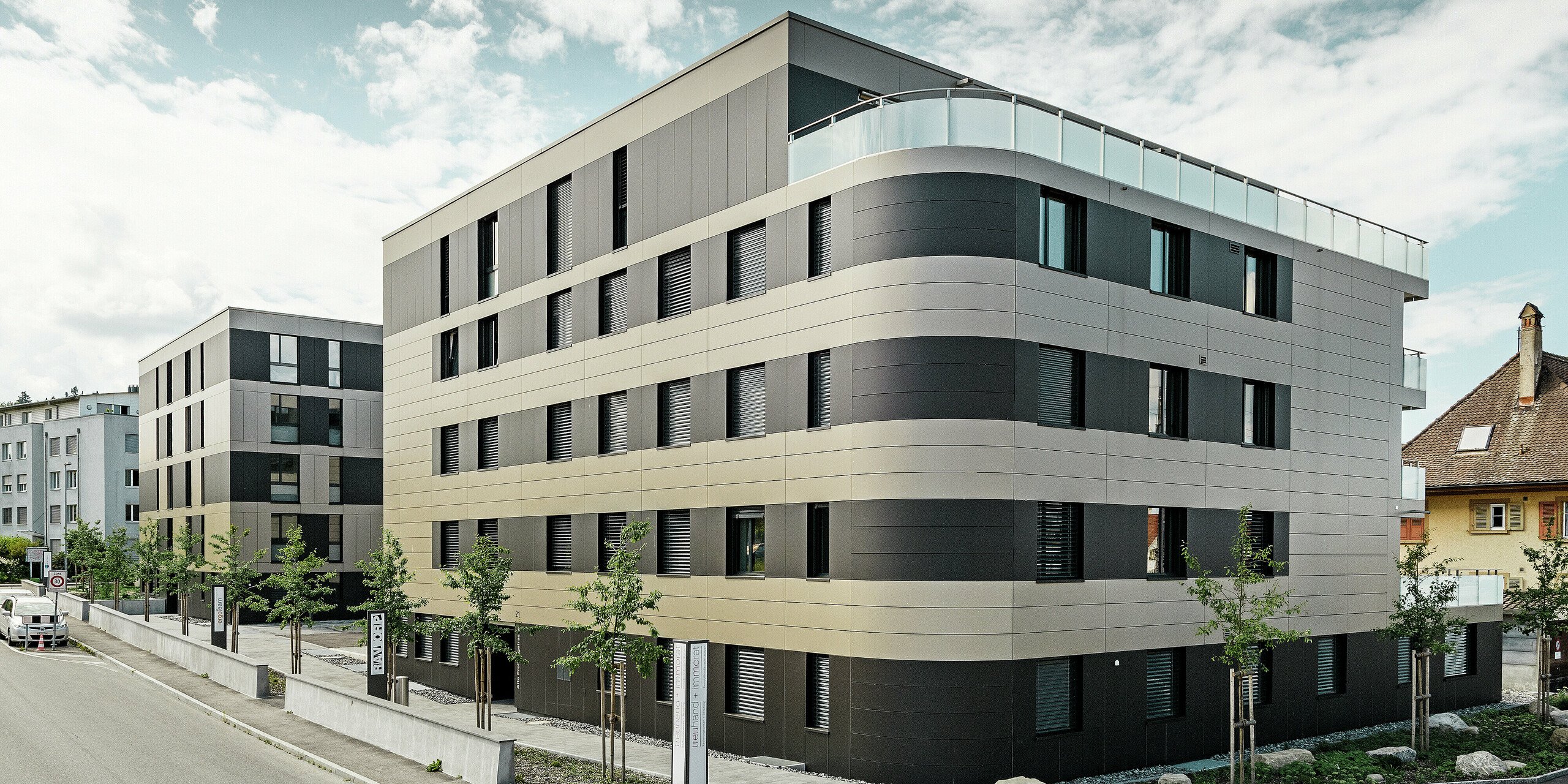 Kockast stanovanjski kompleks z aluminijasto fasado v bronasti barvi in črno-zelenimi elementi