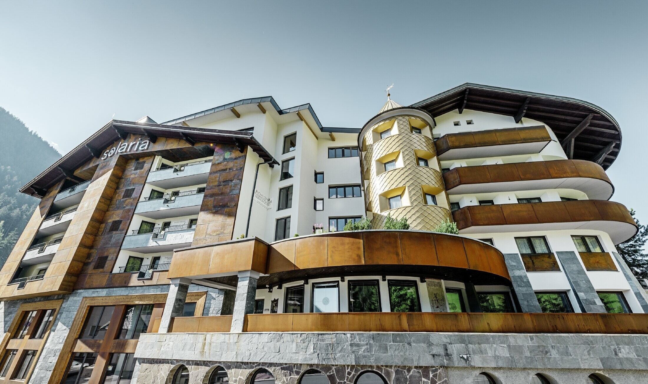 Tradicionalen hotel v kraju Ischgl z lesenimi balkoni in leseno fasado ter stolpom s pozlačenimi aluminijastimi rombi PREFA