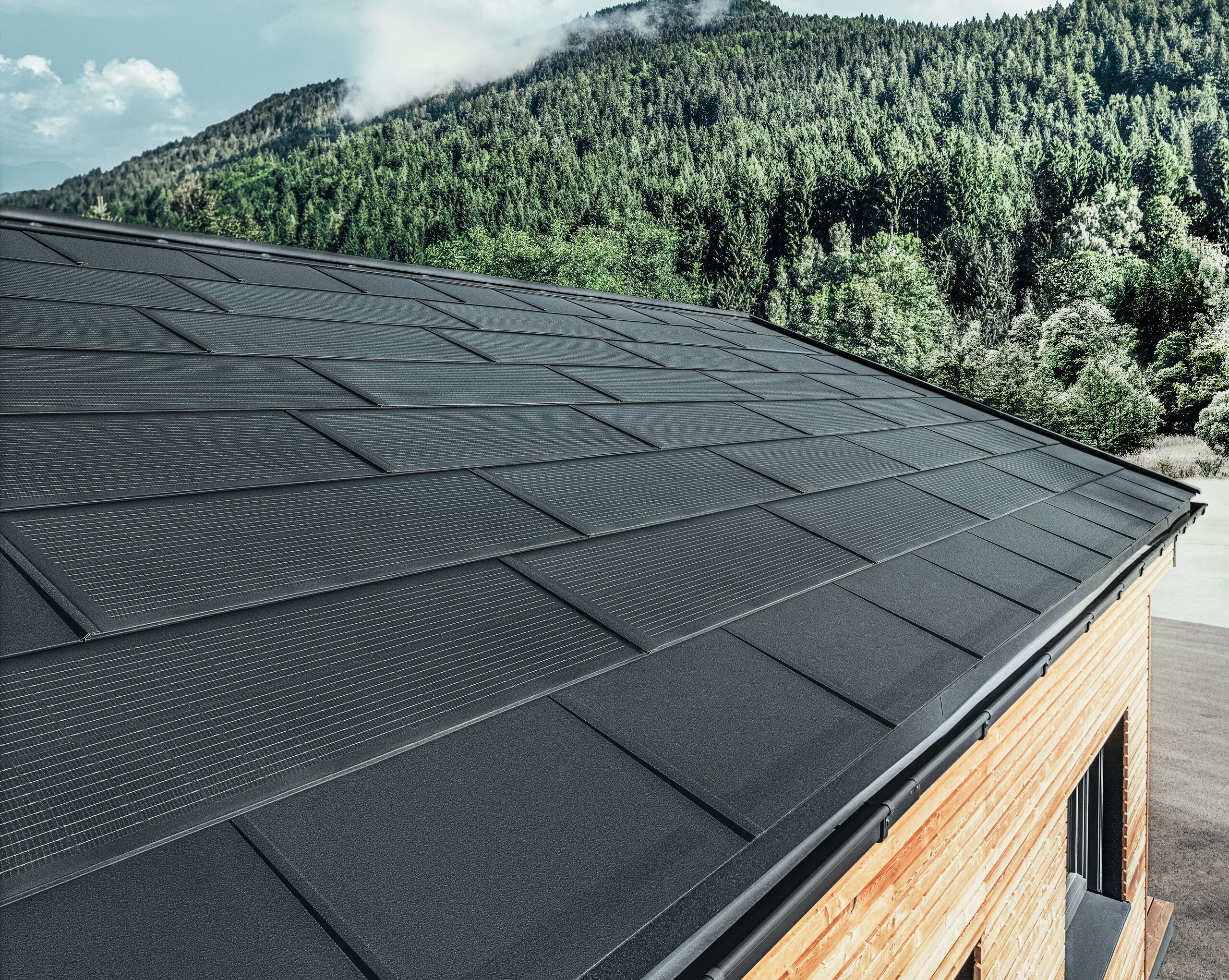 Solarna strešna plošča PREFA v veliki izvedbi v kombinaciji s strešno ploščo R.16 v črni barvi, pravokotnim žlebom in fasado iz macesnovega lesa.
