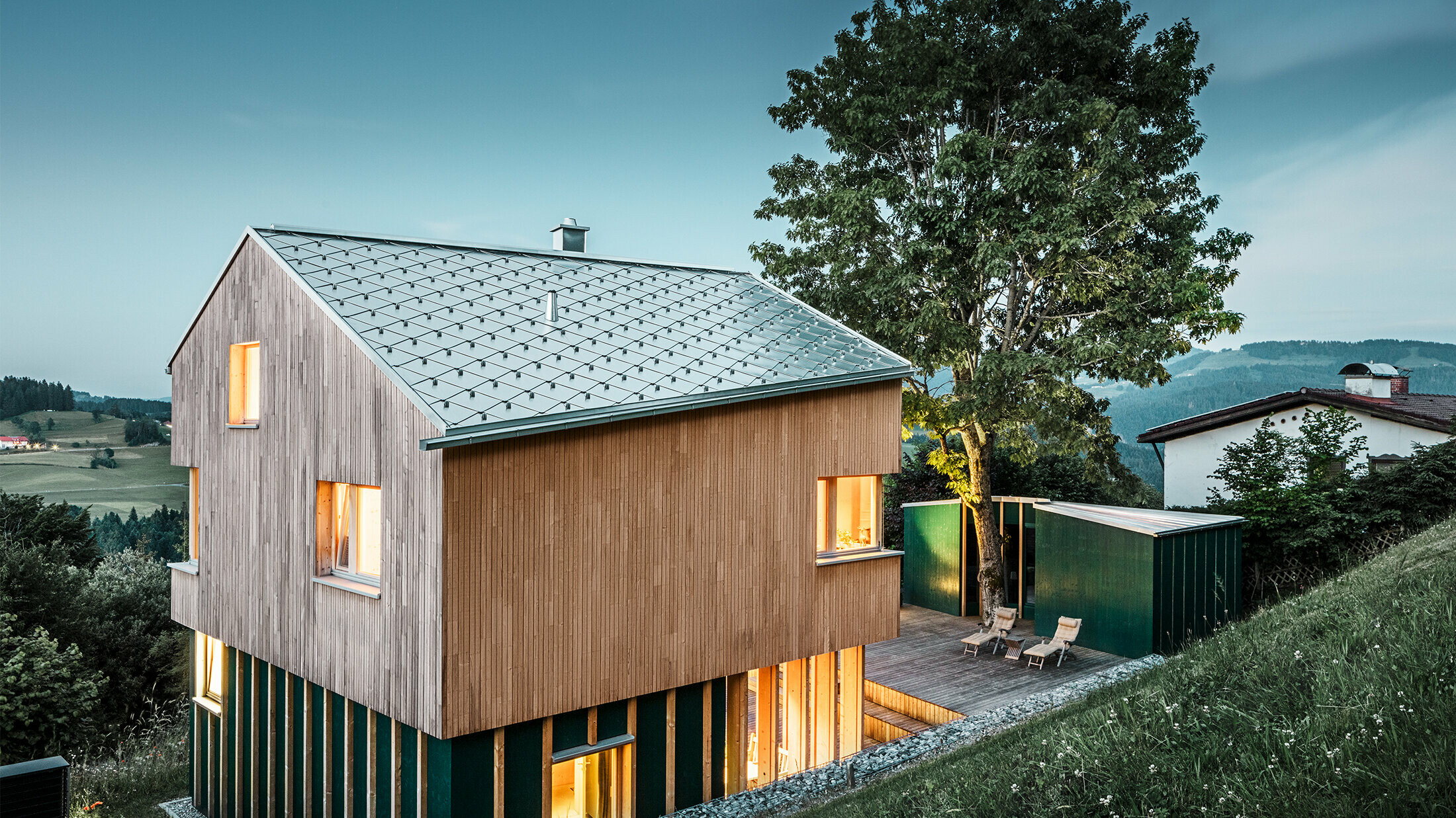 Novo zgrajena družinska hiša z leseno fasado in streho PREFA v barvi naravni aluminij v obliki romba