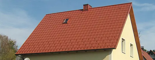 Klasična dvokapna streha z majhnim strešnim oknom in dimnikom, prekrita s PREFA strešno ploščo v opečno rdeči barvi, vključno s snegolovi in varnostnimi kavlji.