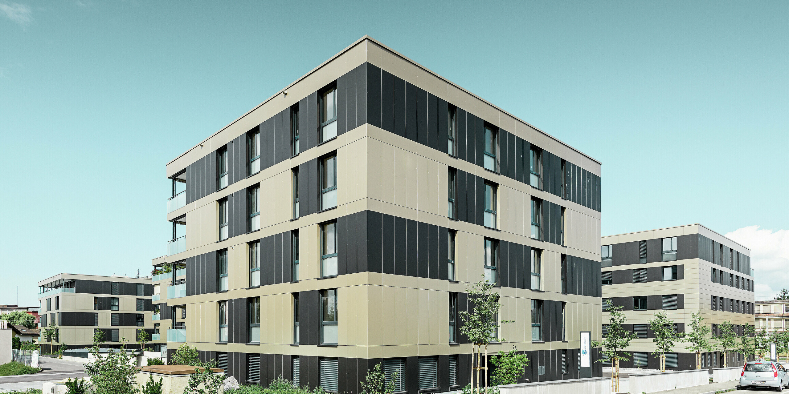 Kockast stanovanjski kompleks z aluminijasto fasado v bronasti barvi in črno-zelenimi elementi